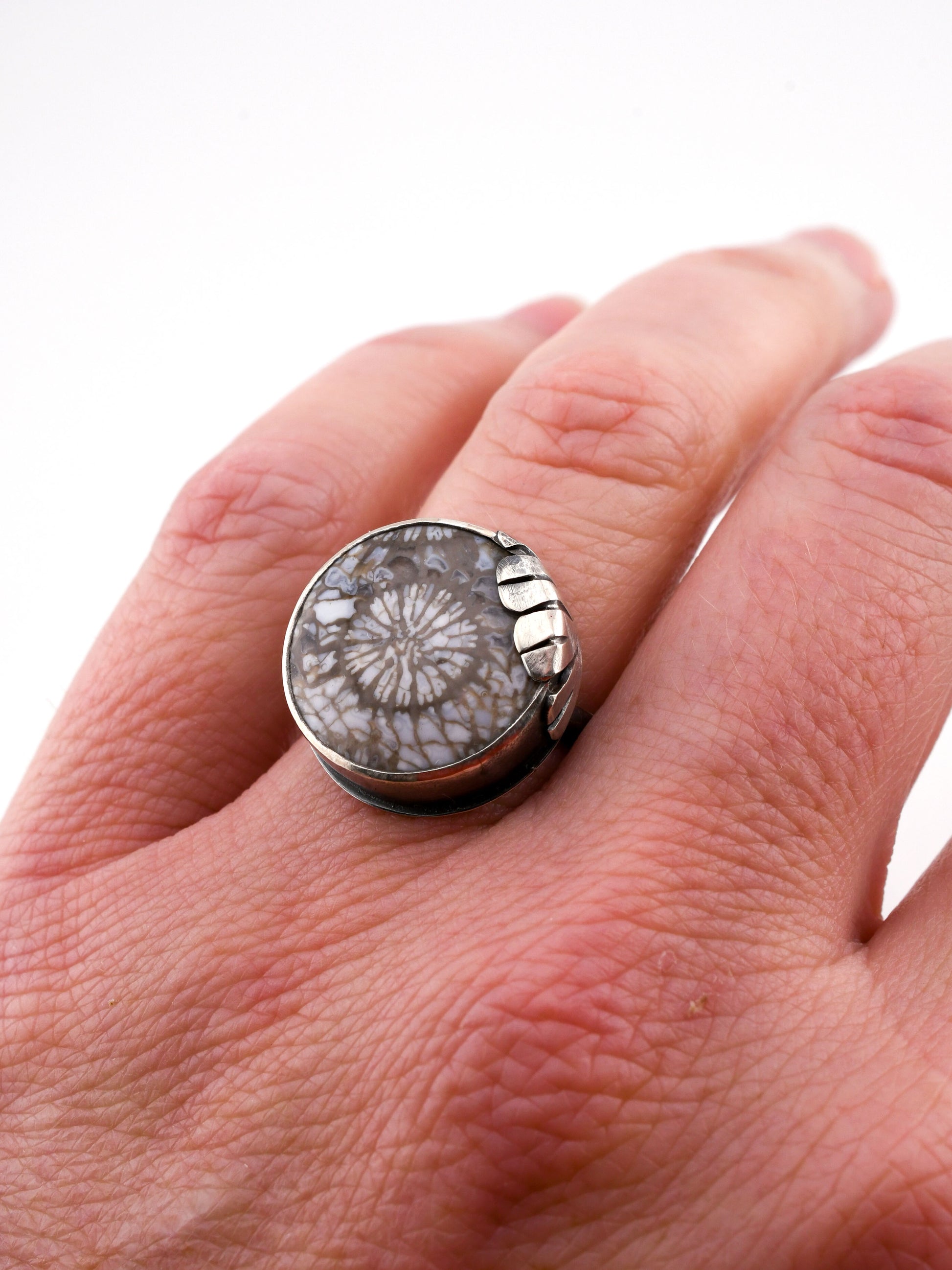 Close-up of a hand wearing a ring with a textured stone design on a white background