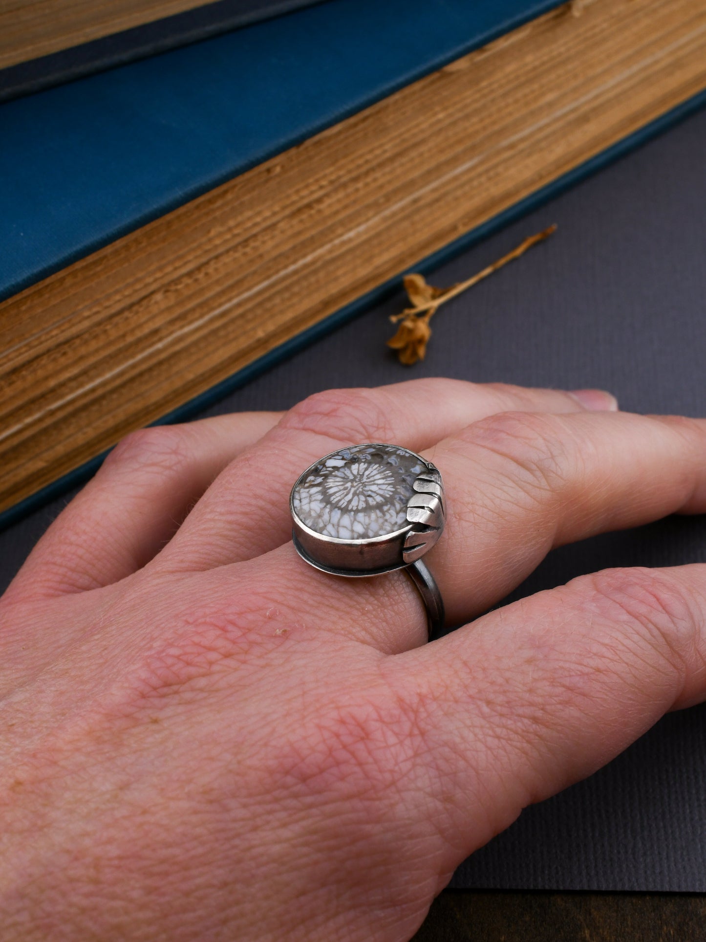 Close-up of a hand wearing a silver ring with a floral design, set against a book background.