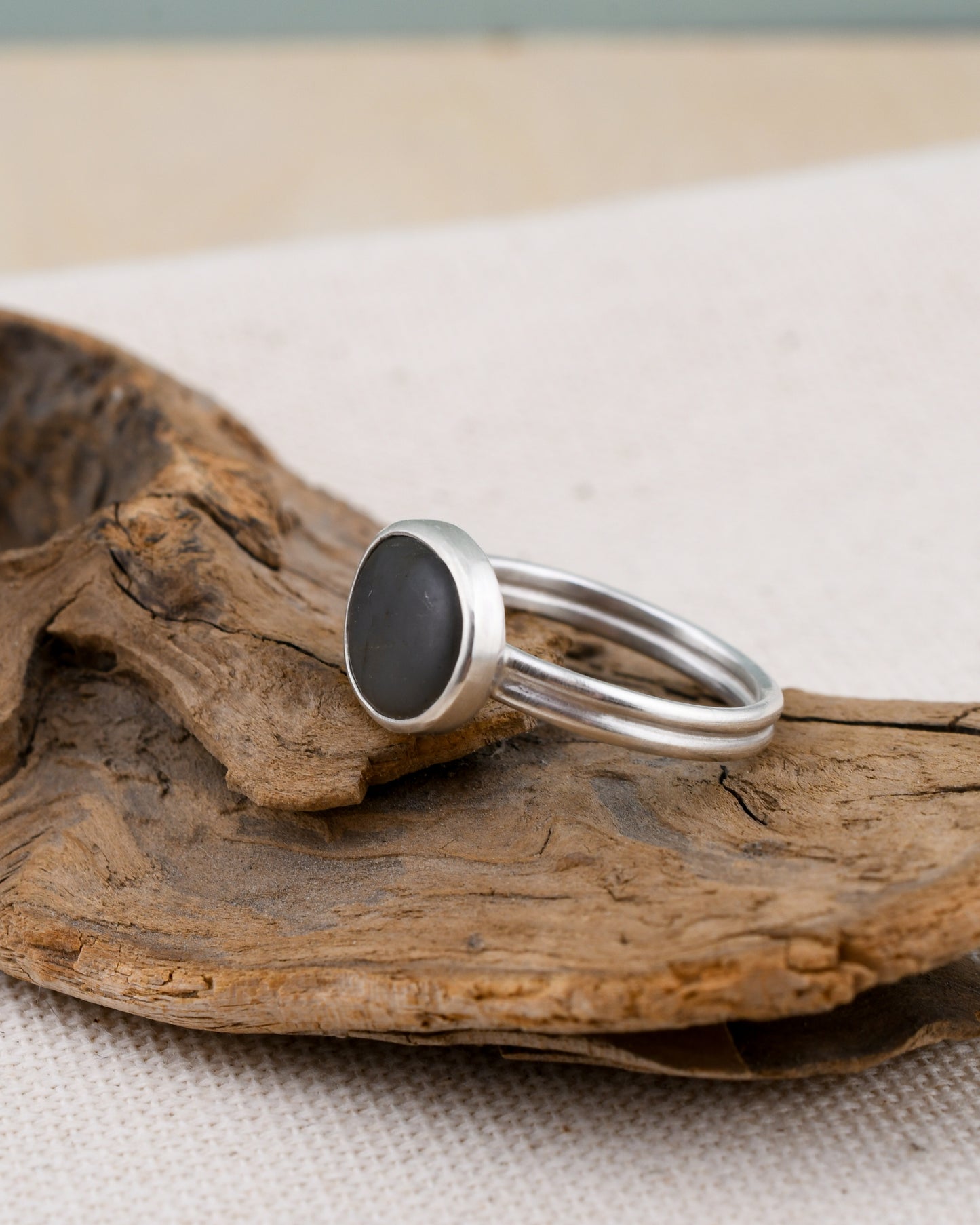 Silver ring with a dark stone on a piece of driftwood