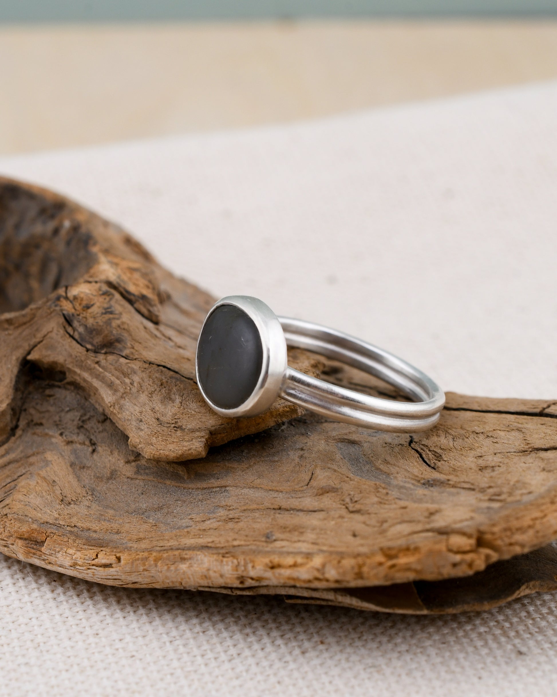 Silver ring with a dark stone on a piece of driftwood