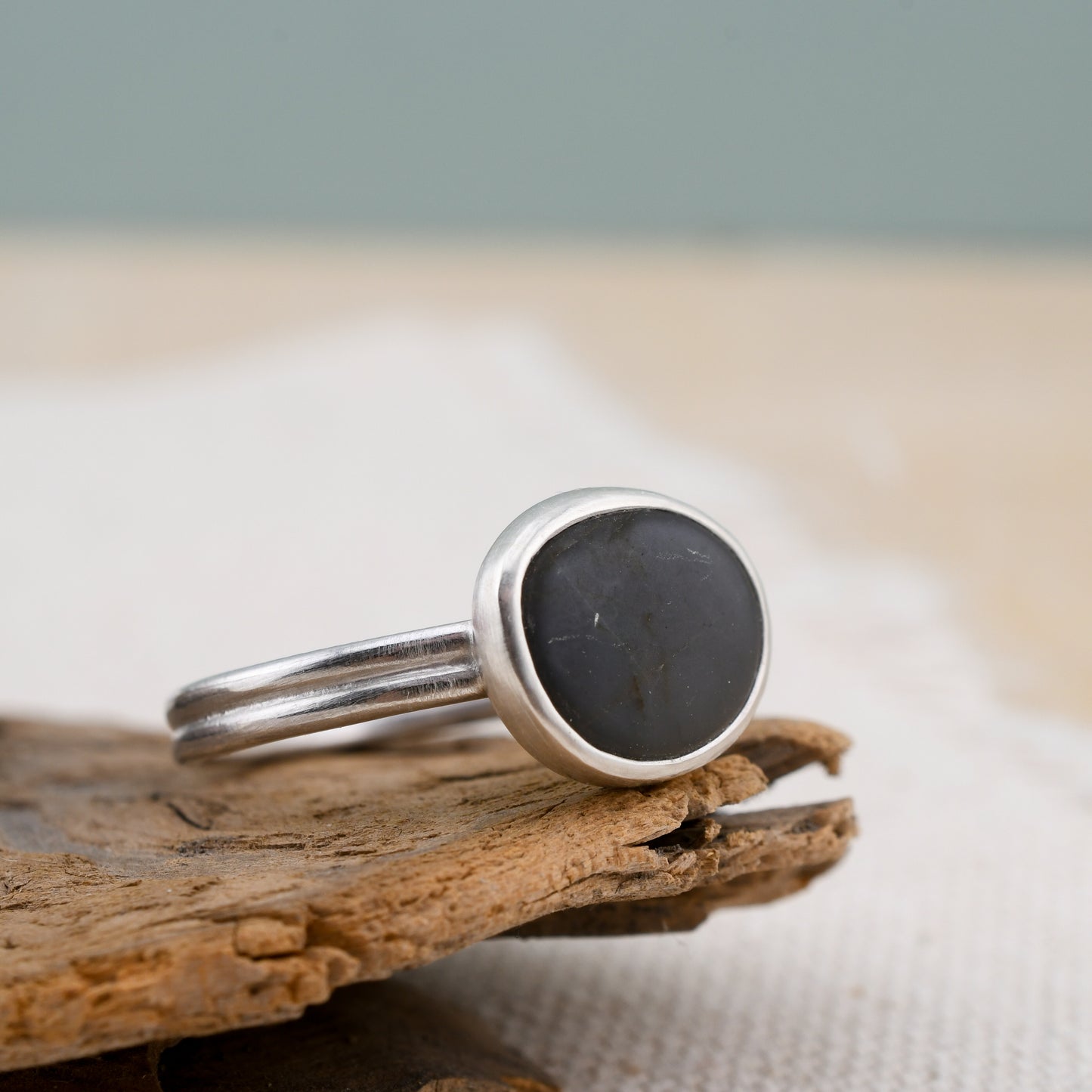 Silver ring with a dark gray beach stone on a wooden surface