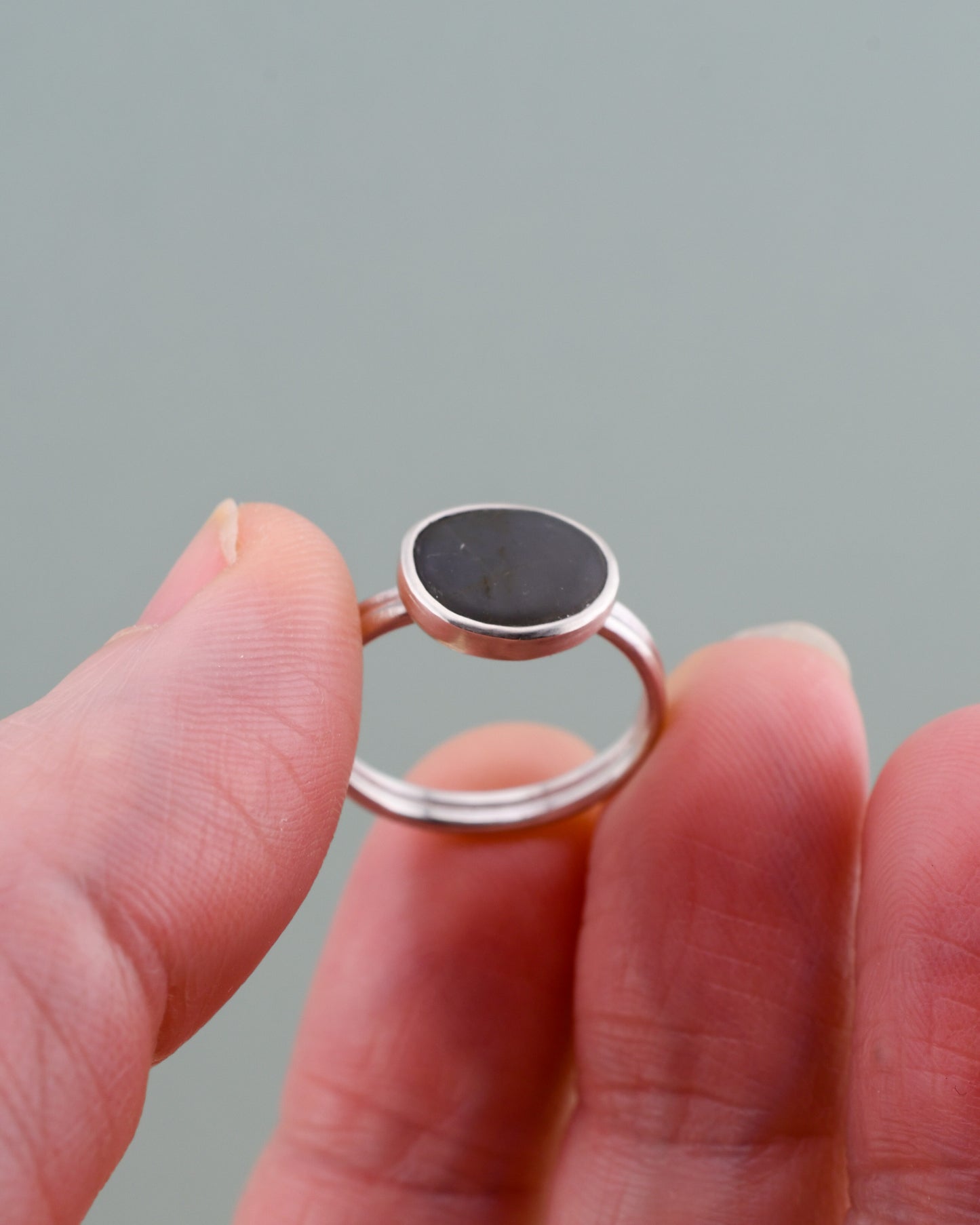 Silver ring with a dark gray stone held between fingers against a light gray background