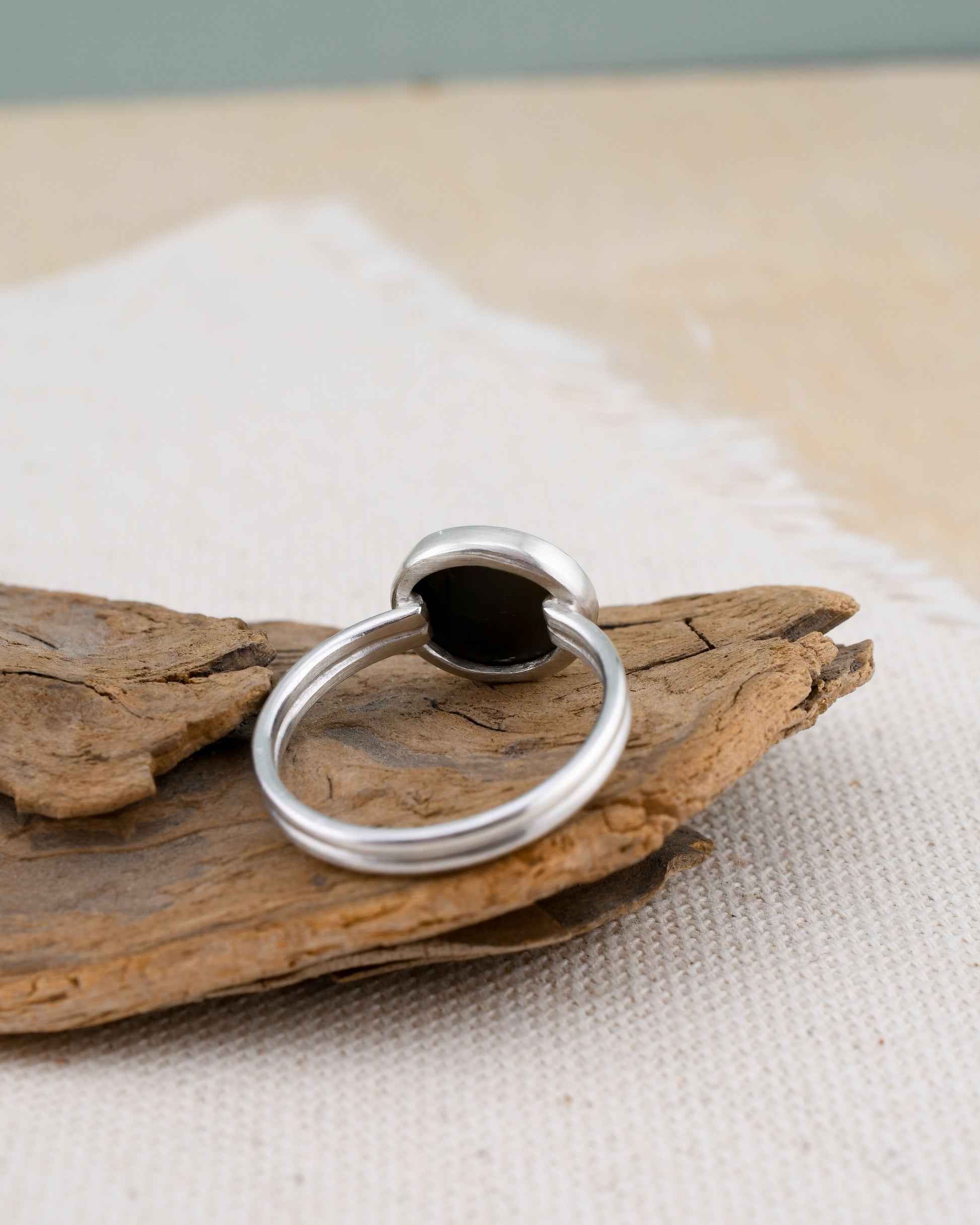 backside of a silver ring with a dark gray beach stone on a piece of driftwood