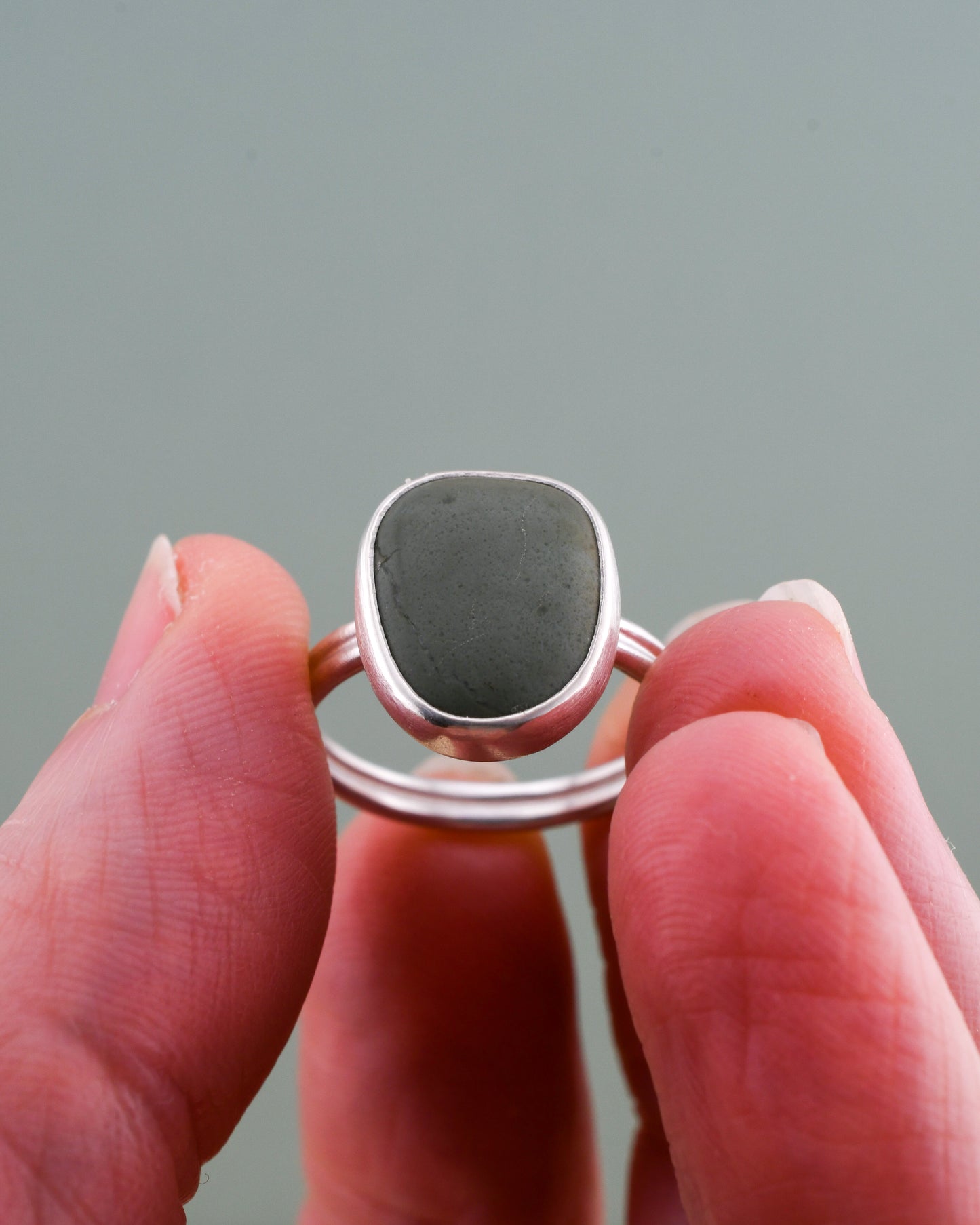 Ring with a storm blue stone held between fingers against a gray background