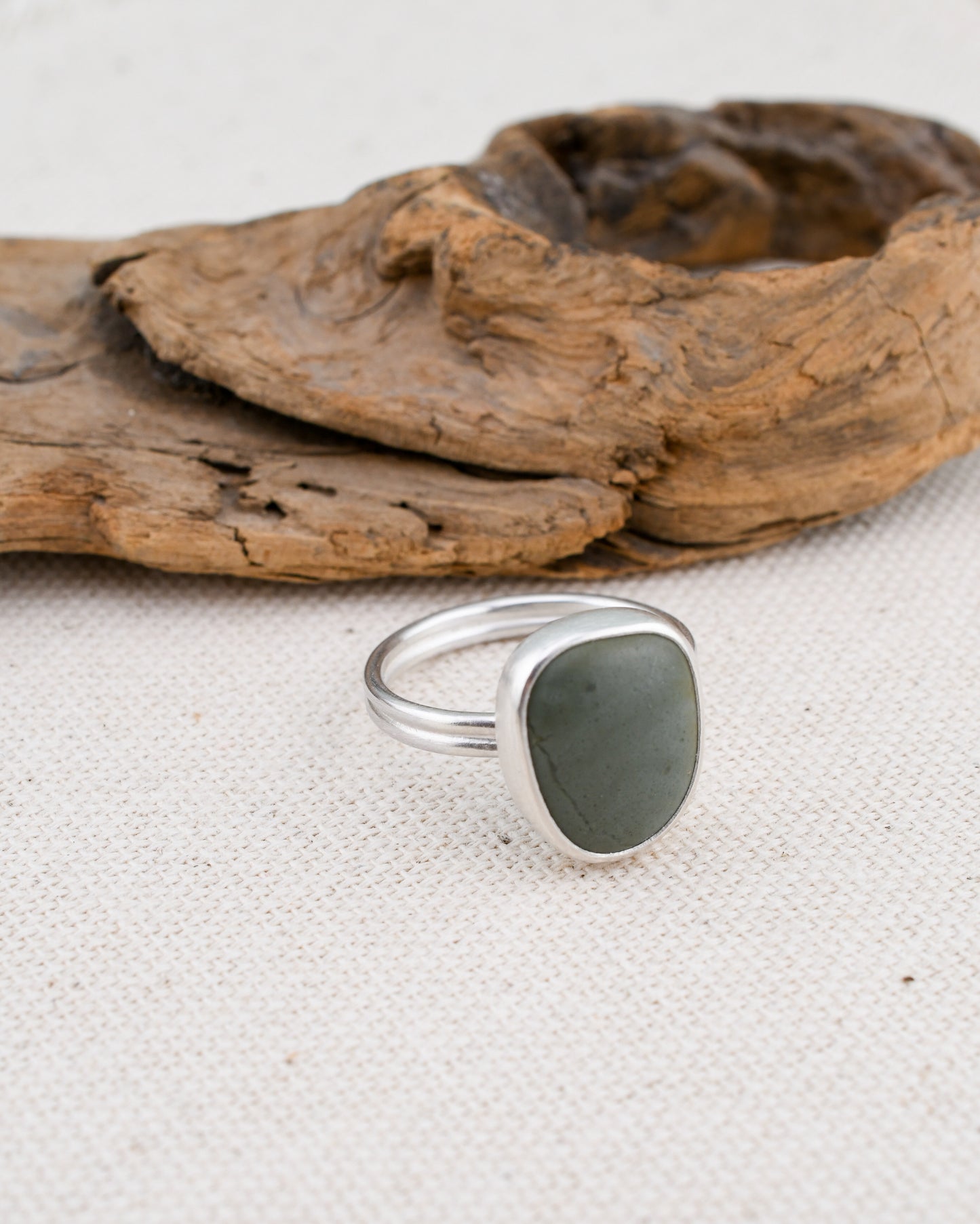 Silver ring with a gray-blue stone on a textured surface with driftwood
