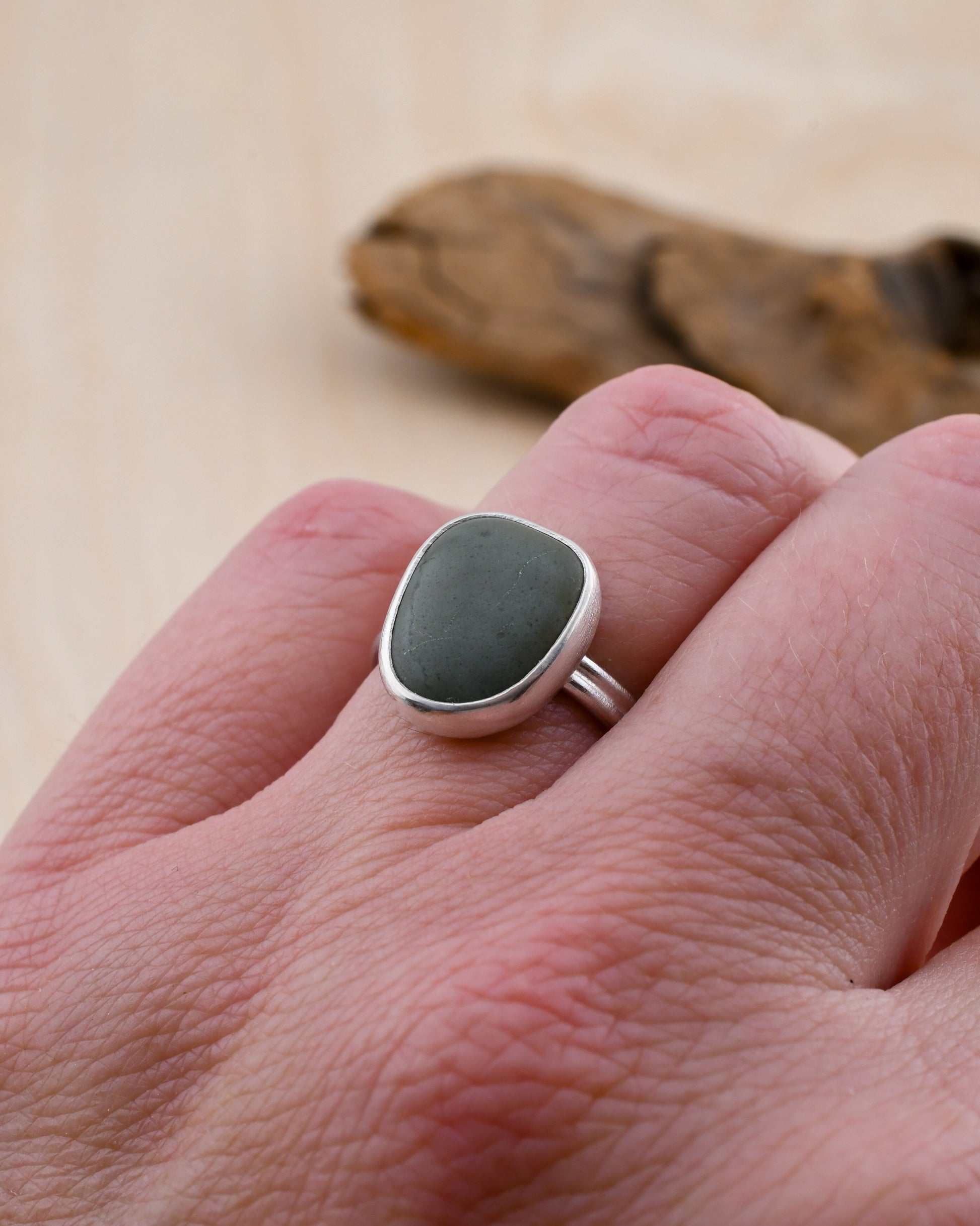 Silver ring with a storm blue beach stone on a hand, with a wooden background