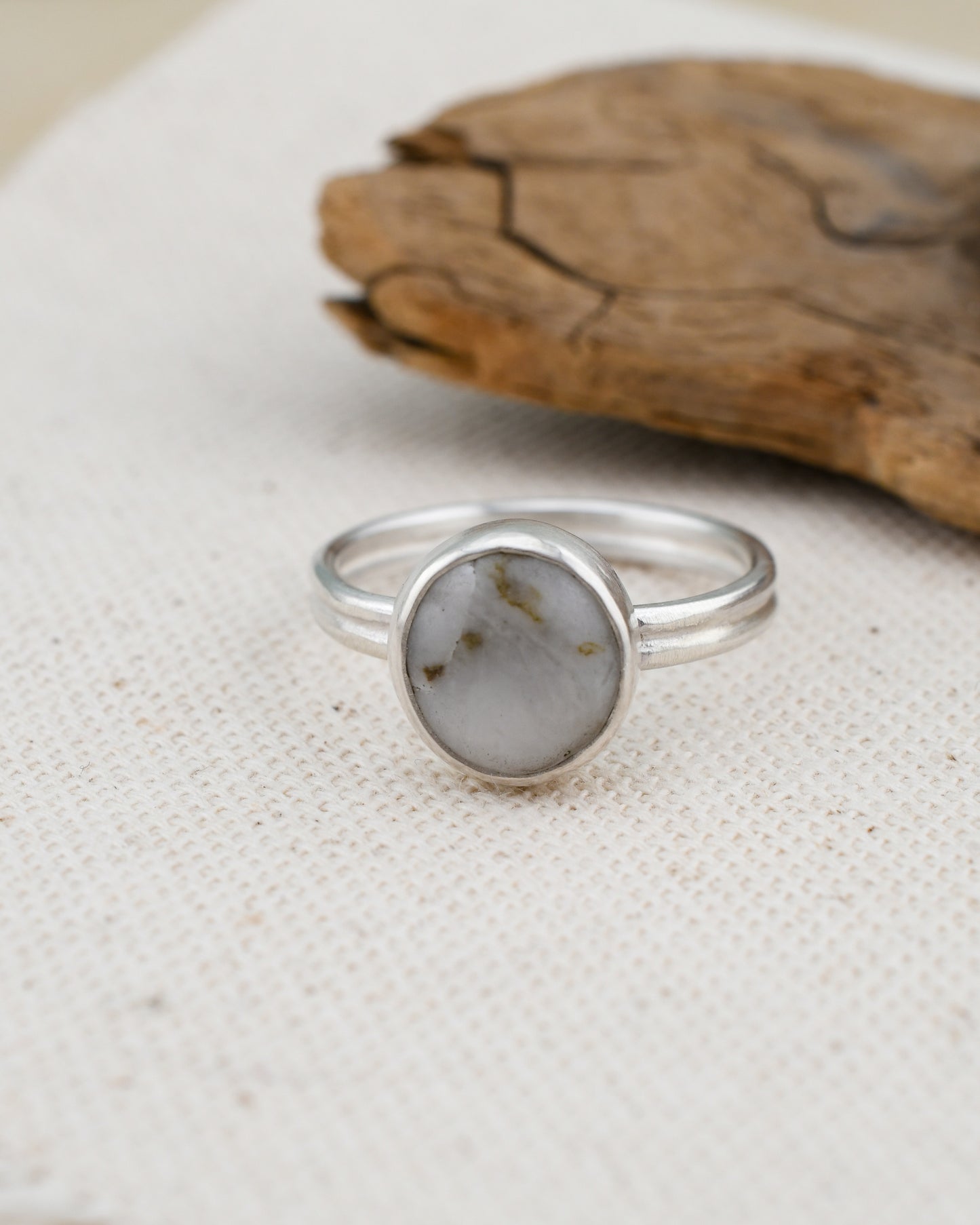 Silver ring with a  white beach stone on a textured surface with wooden piece