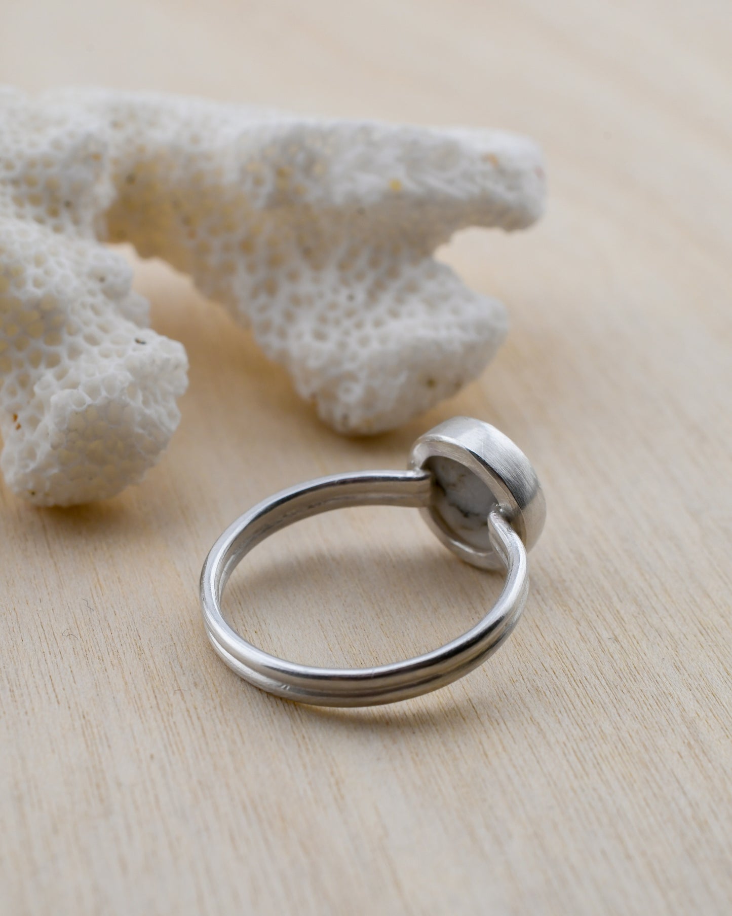 Backside of a silver ring on a light wooden surface with white coral in the background