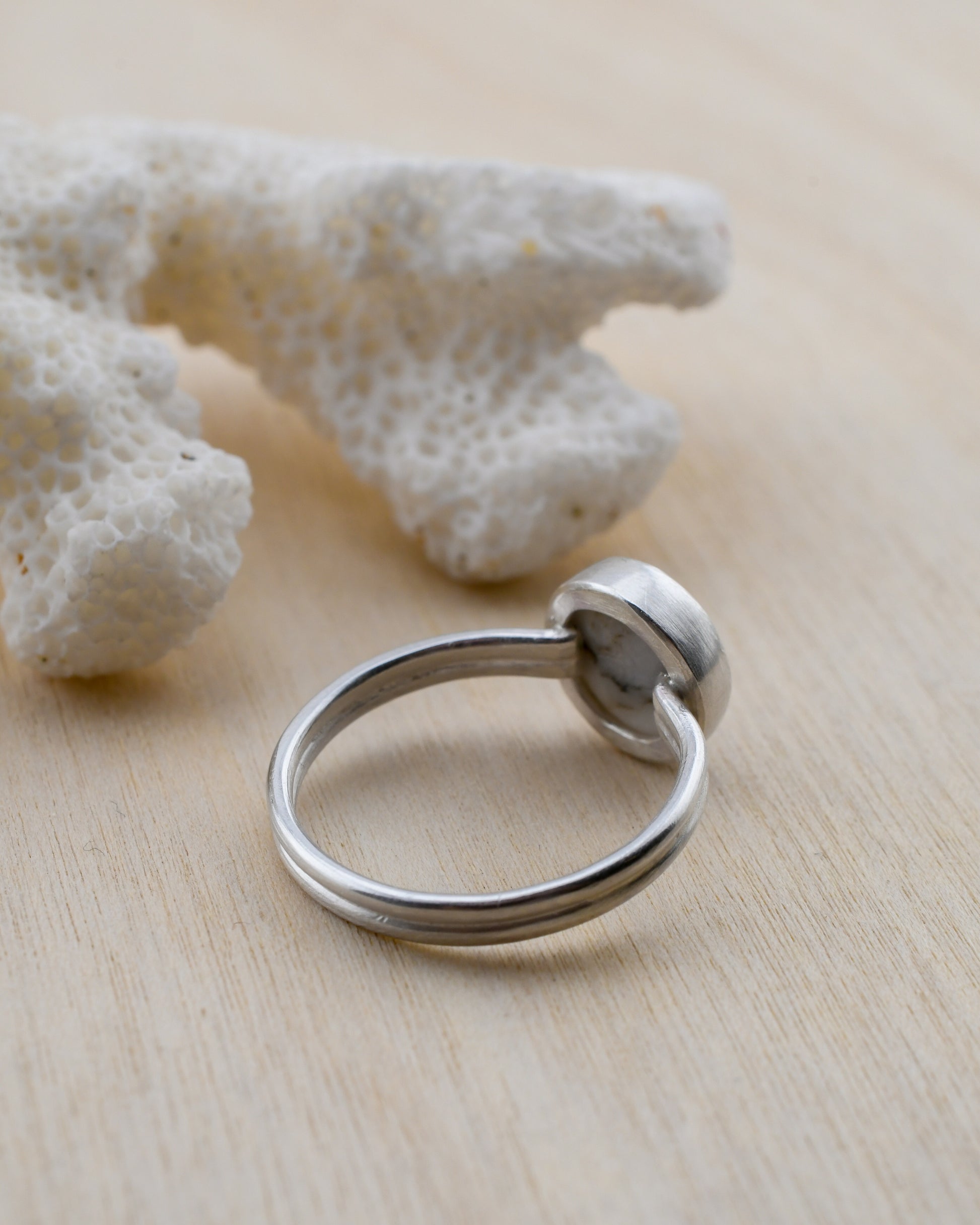 Backside of a silver ring on a light wooden surface with white coral in the background