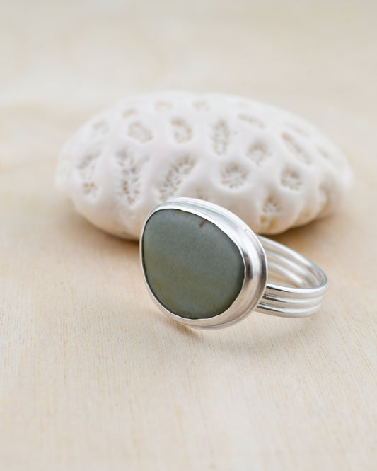 Silver ring with a storm blue beach stone on a beige surface with a white coral in the background