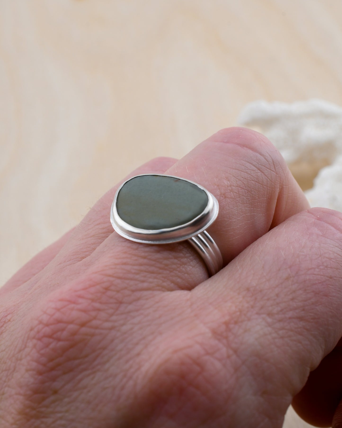Silver ring with a storm blue stone on a person's finger against a neutral background