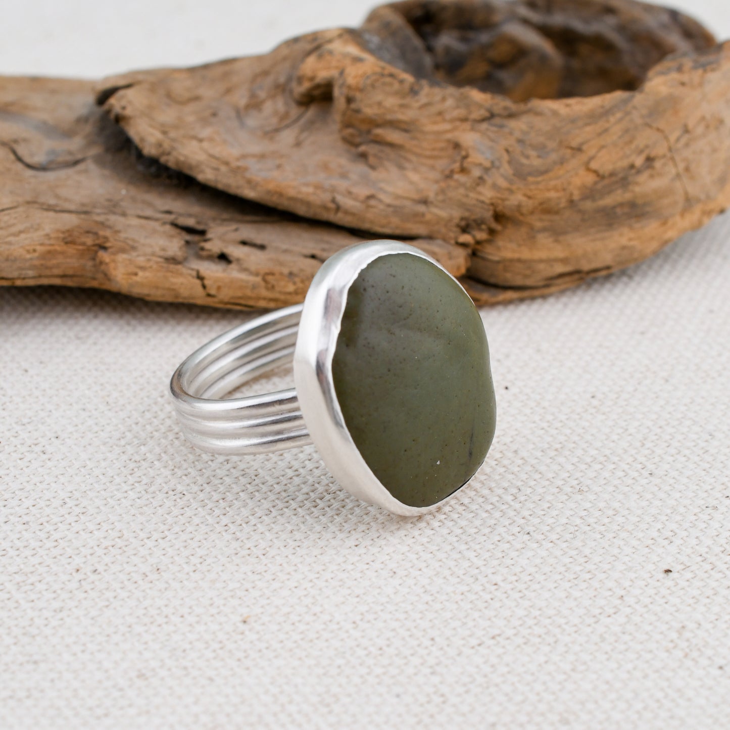 Silver ring with a green stone on a textured surface with driftwood.