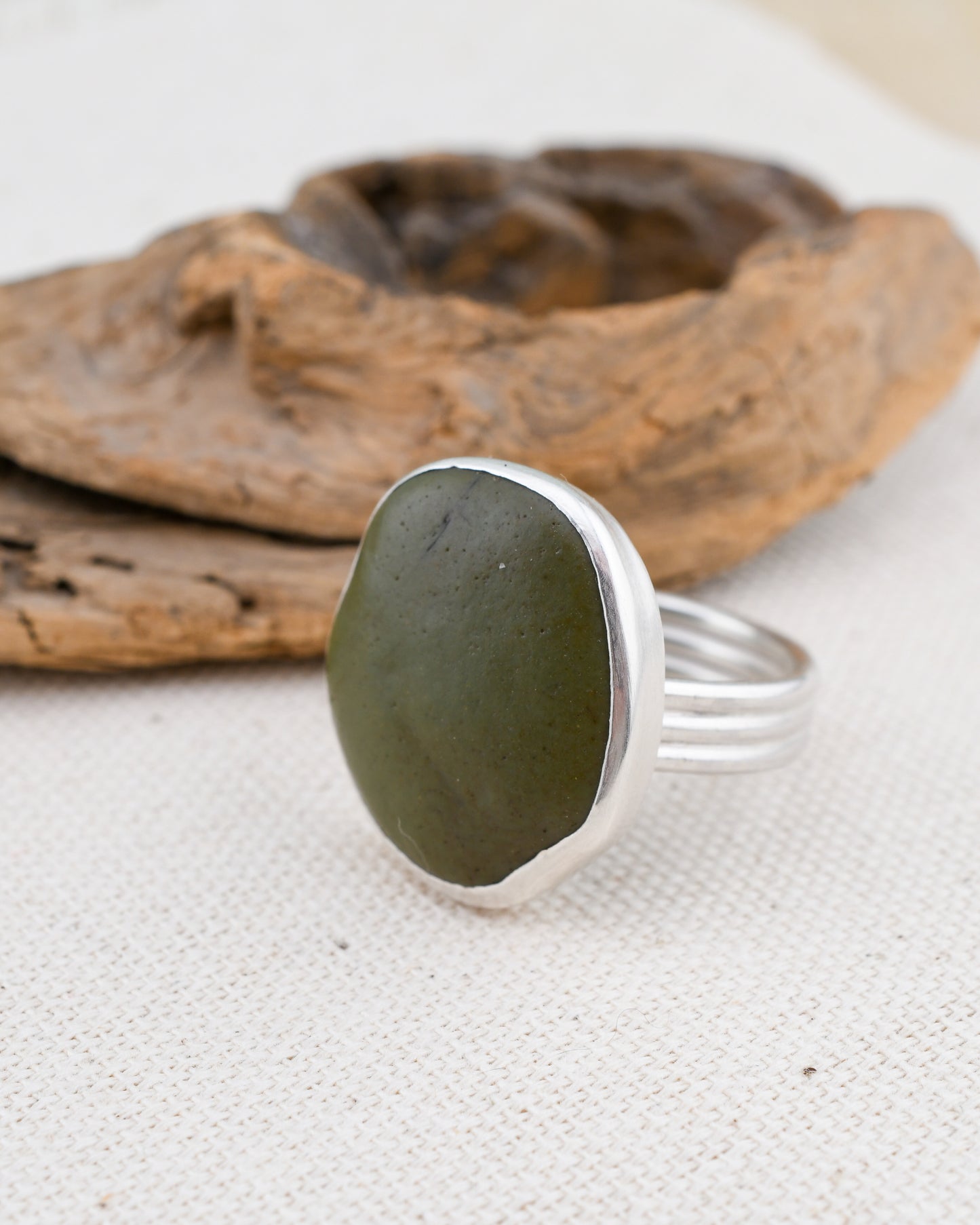 Ring with green stone and silver band on a textured surface with wooden elements.