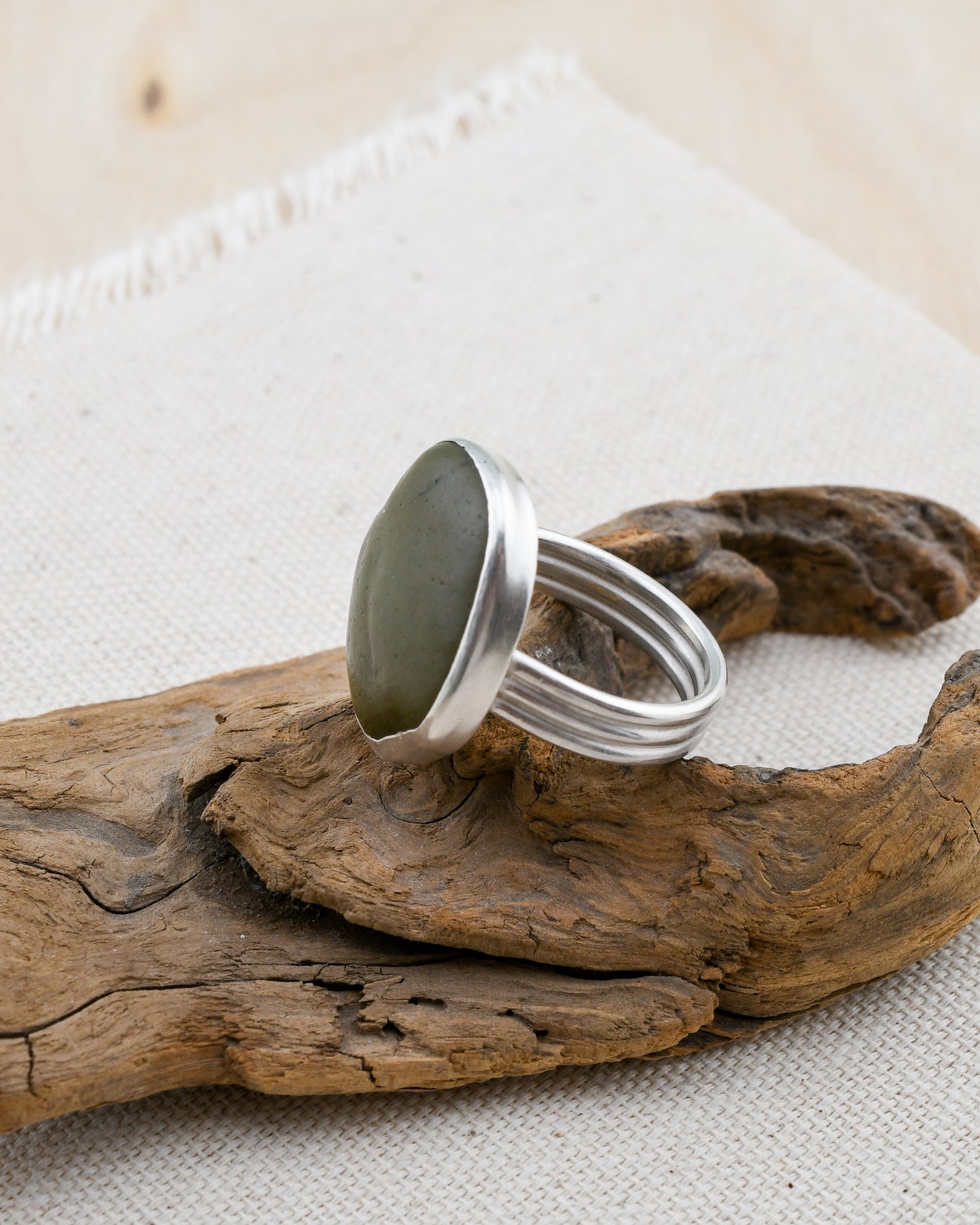 Silver ring with a green beach stone on a piece of driftwood