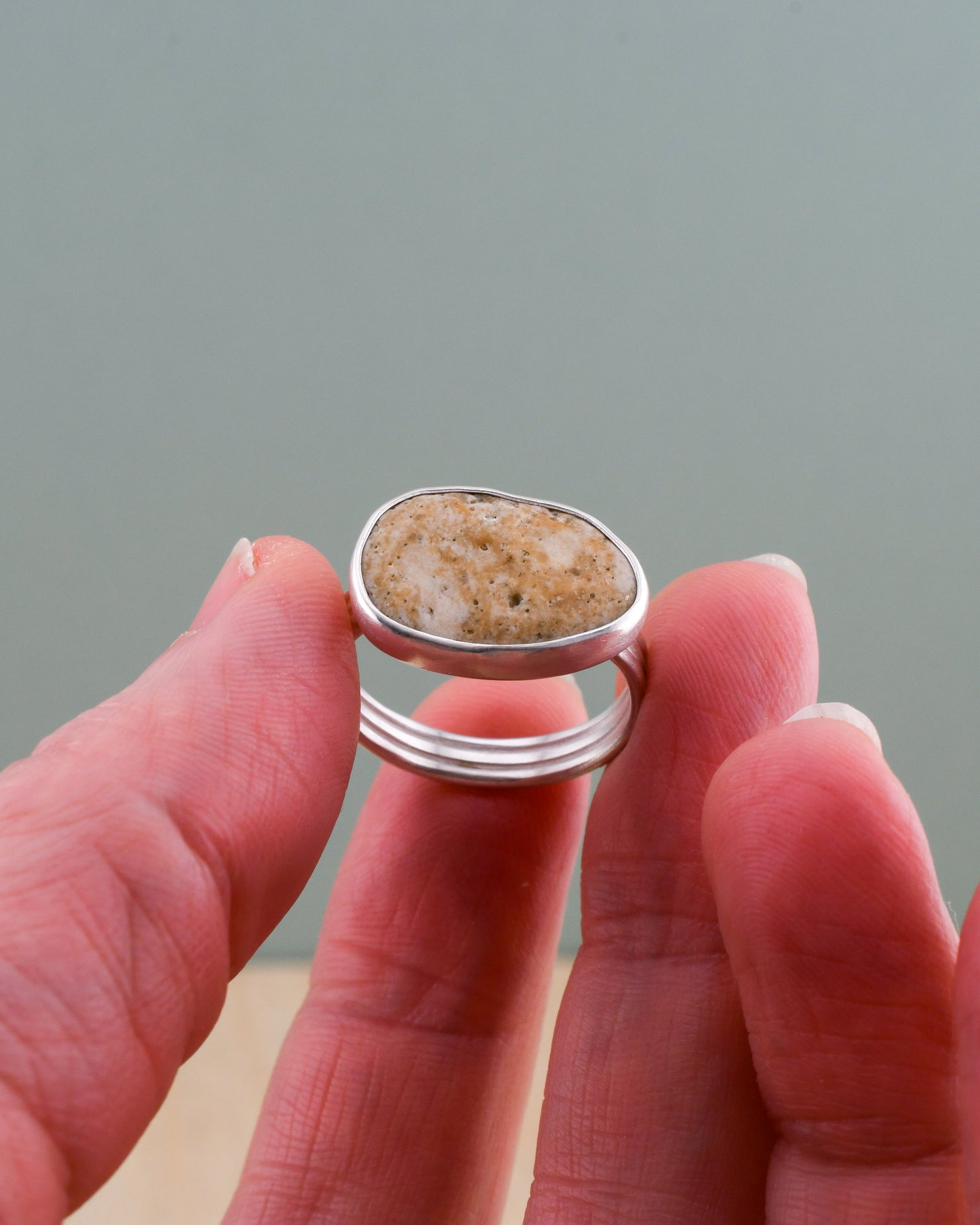 Hand holding a silver ring with a natural stone design against a gray background