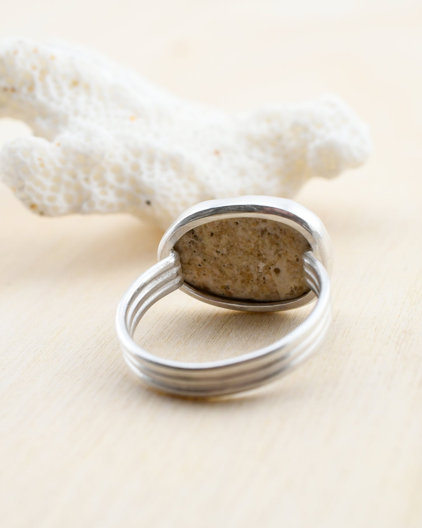 Backside of a silver ring with a stone on a beige background