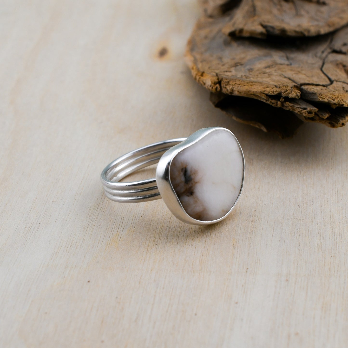 Silver ring with a white beach stone on a beige surface with a piece of driftwood.
