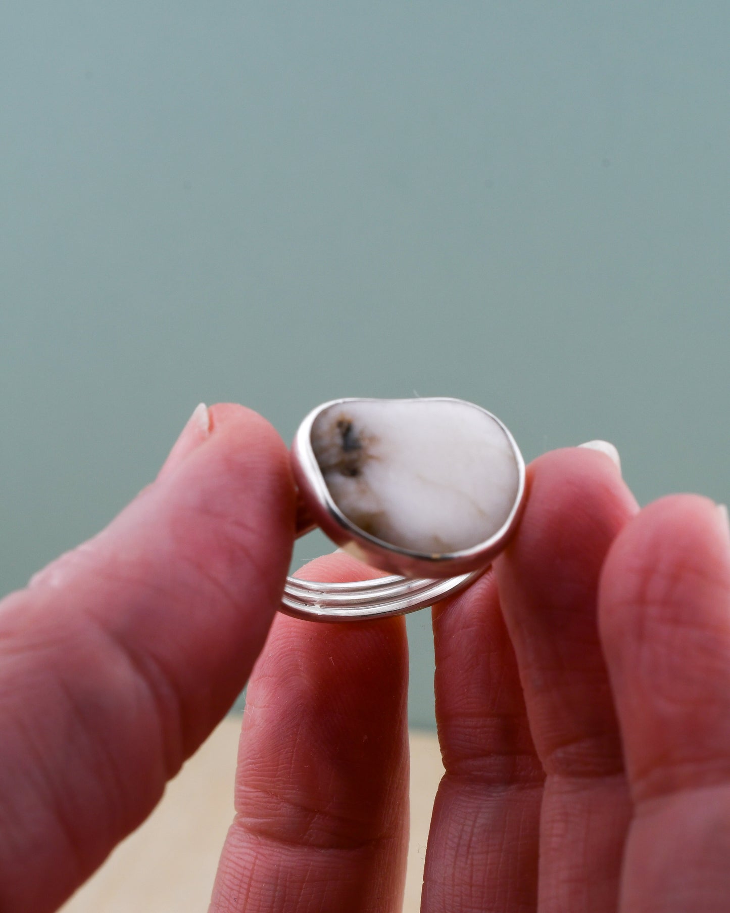 Hand holding a silver ring with a large white beach stone against a neutral background