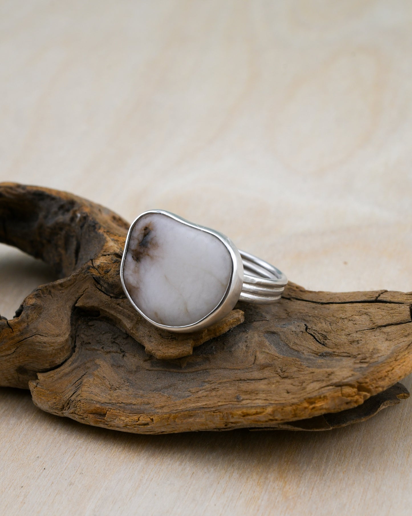 Silver ring with a large beach stone on a piece of driftwood against a beige background