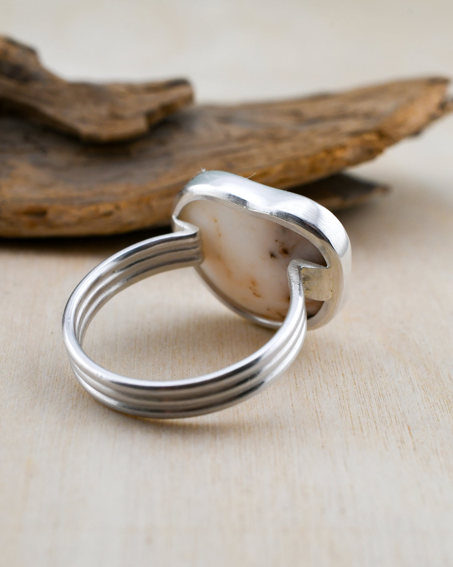 Closeup of backside of silver and beach stone ring with driftwood and a neutral background