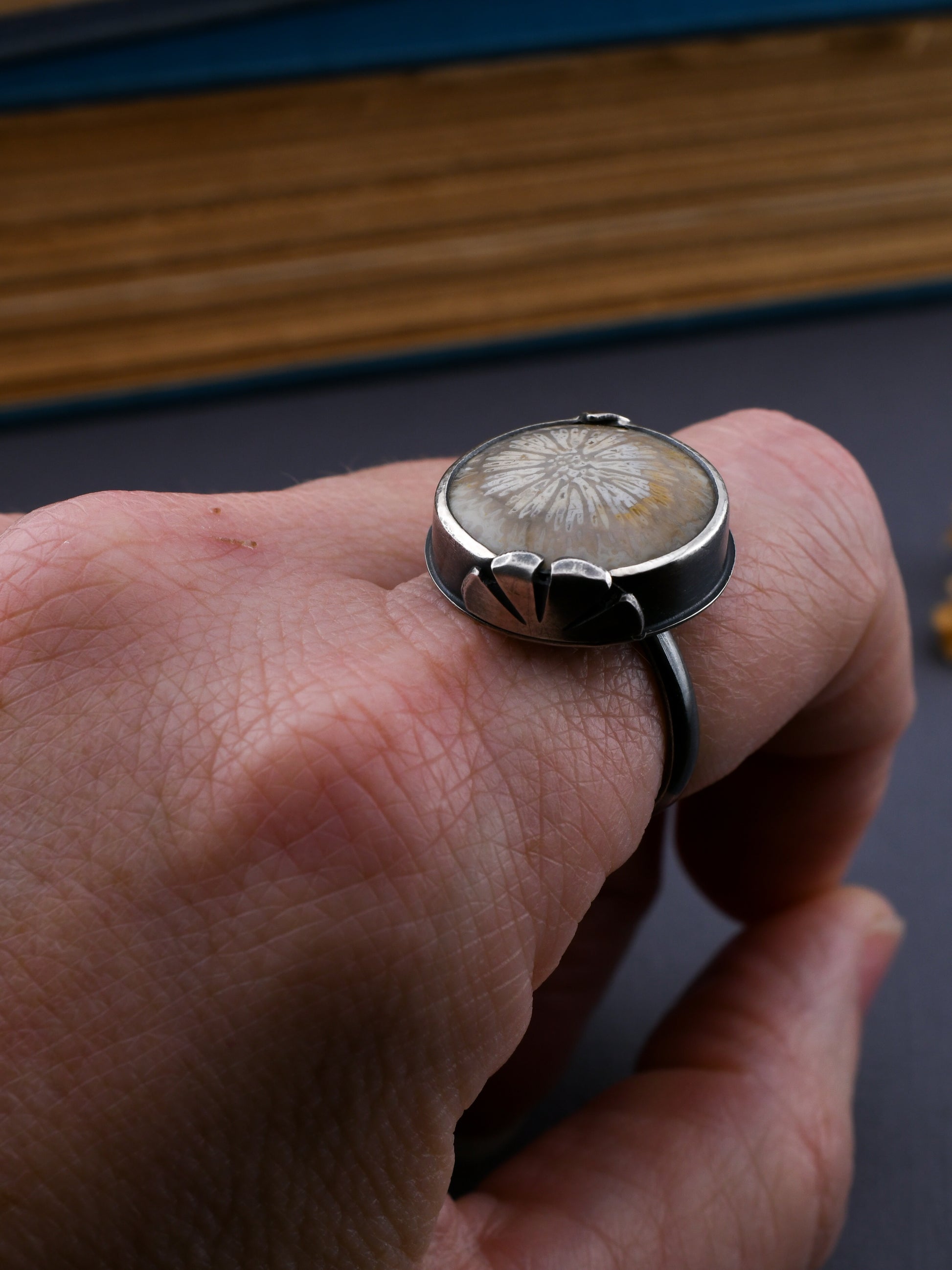 Silver ring with a floral design on a finger against a dark background