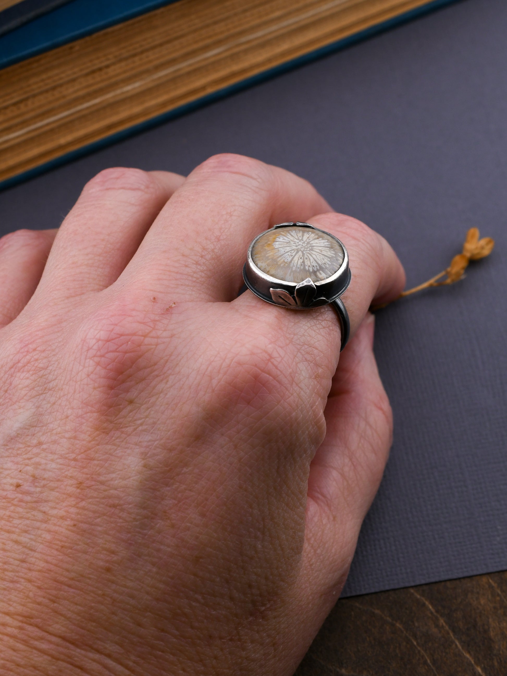 Hand wearing a ring with a floral design on a dark surface