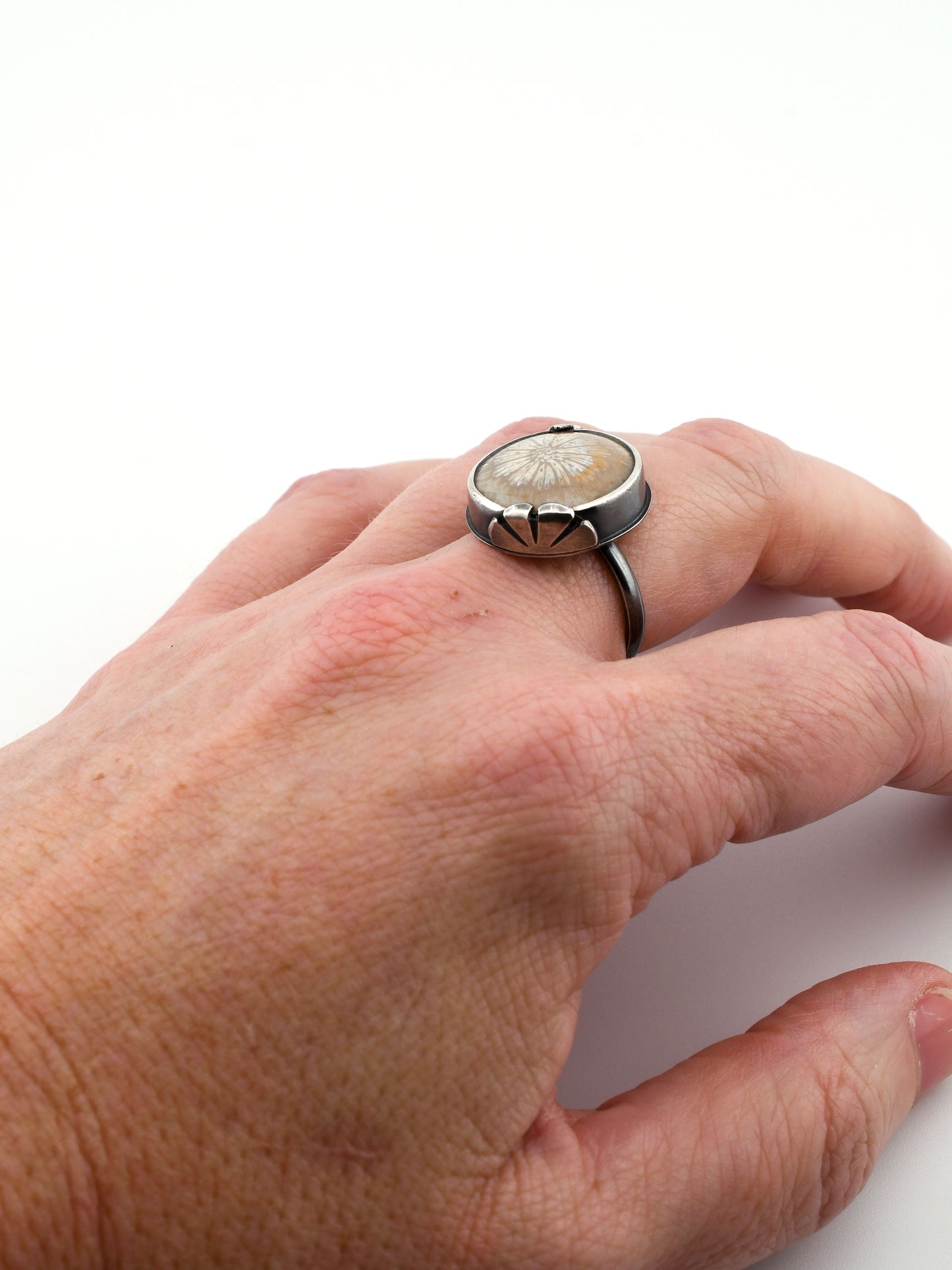 Hand wearing a ring with a circular stone on a white background