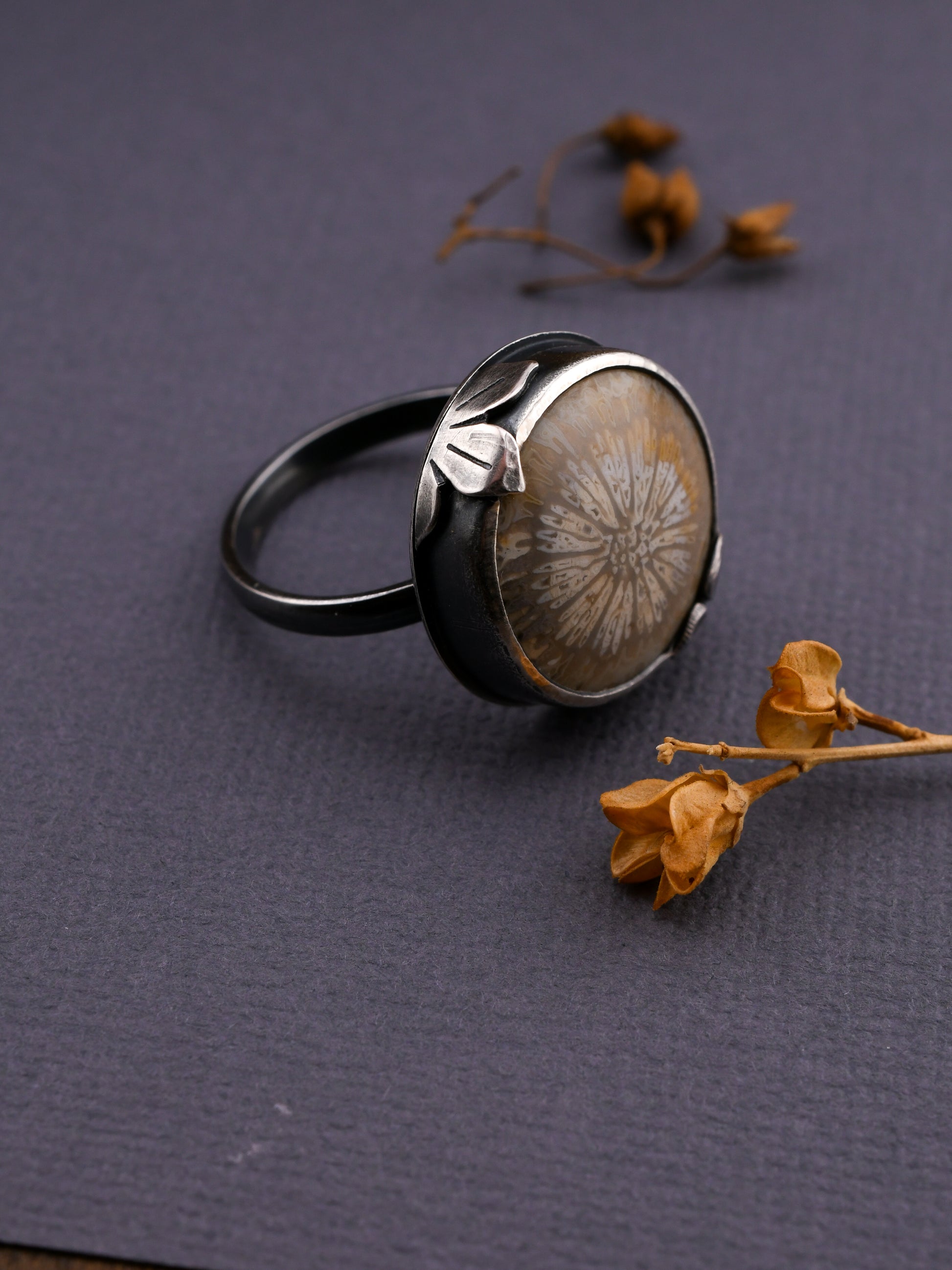 Black ring with a floral design on a dark surface with dried flowers.