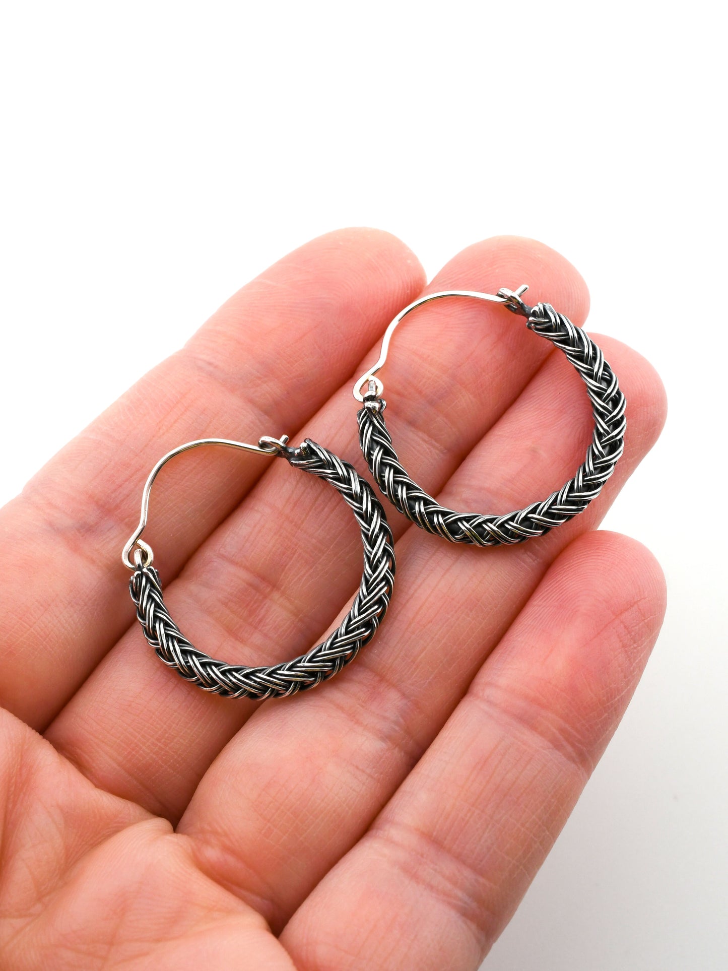 Silver hoop earrings with braided design held in a hand against a white background