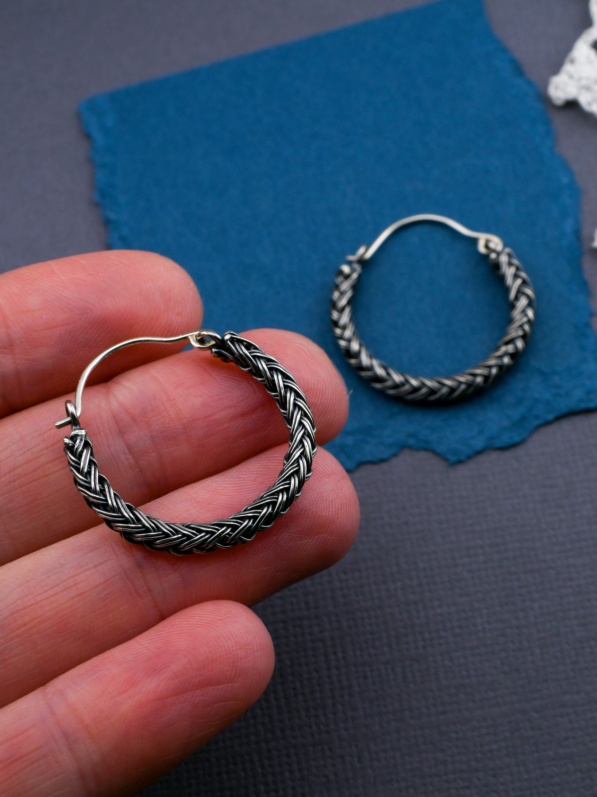 Silver hoop earrings held in a hand with a blue cloth in the background