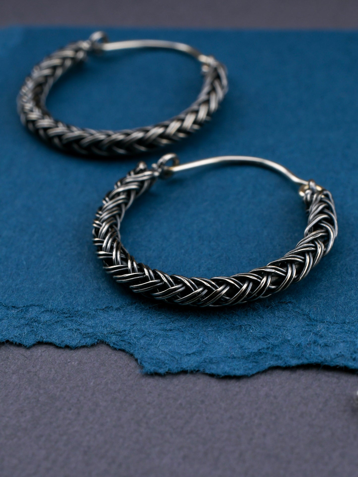 Silver hoop earrings with braided design on a blue background