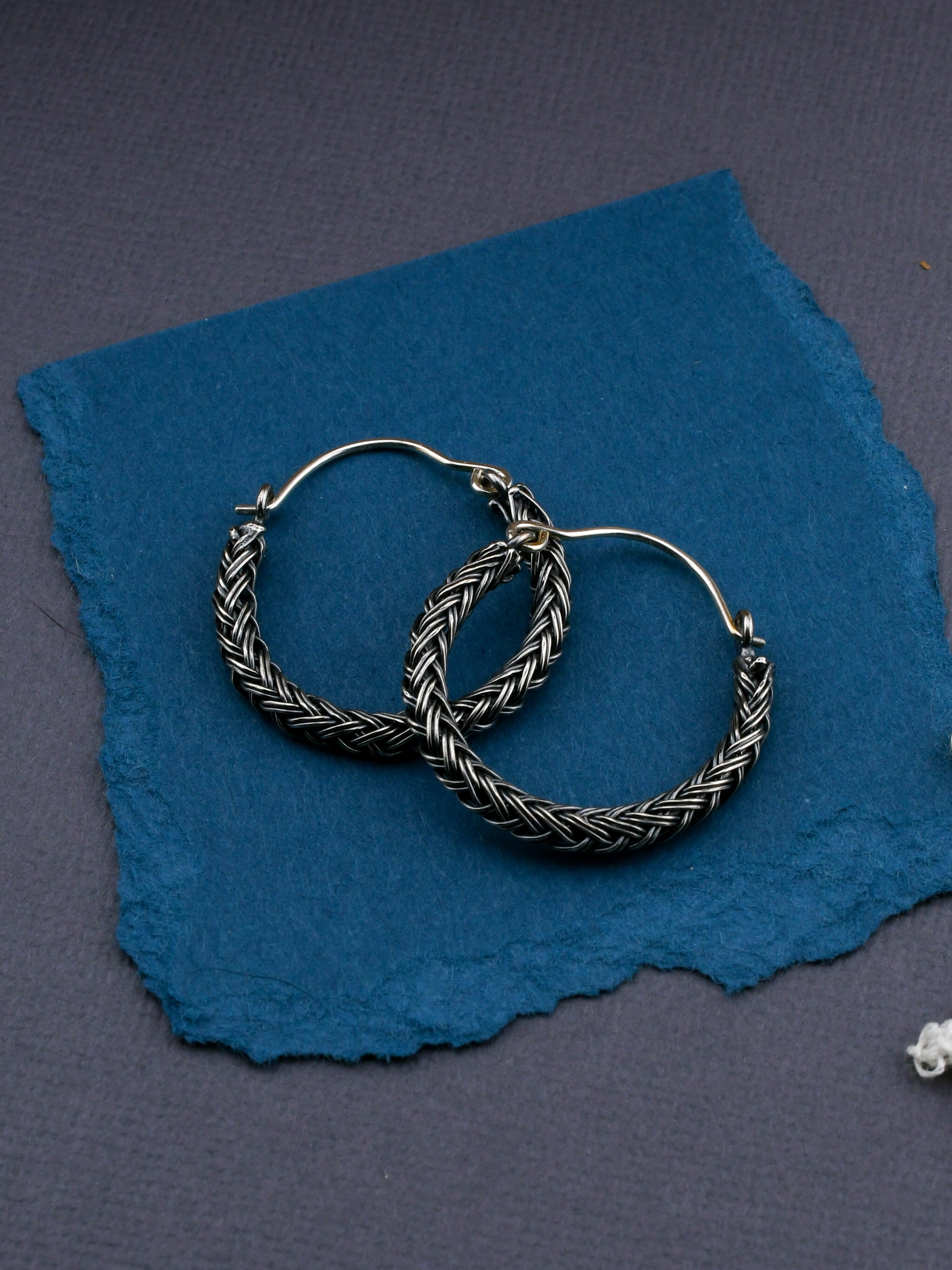 Silver hoop earrings with braided design on a blue textured fabric background