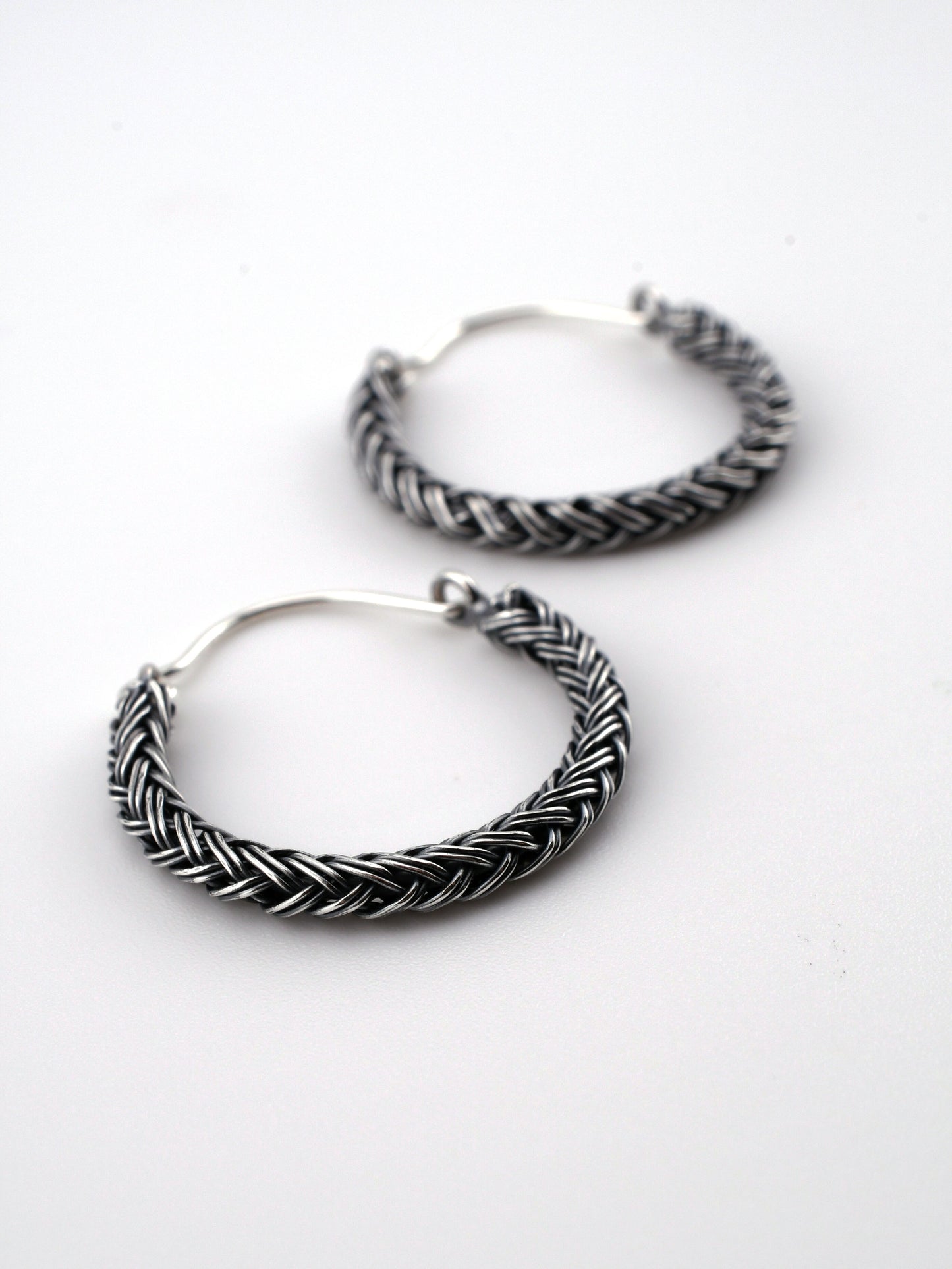 Pair of silver hoop earrings with braided design on a white background