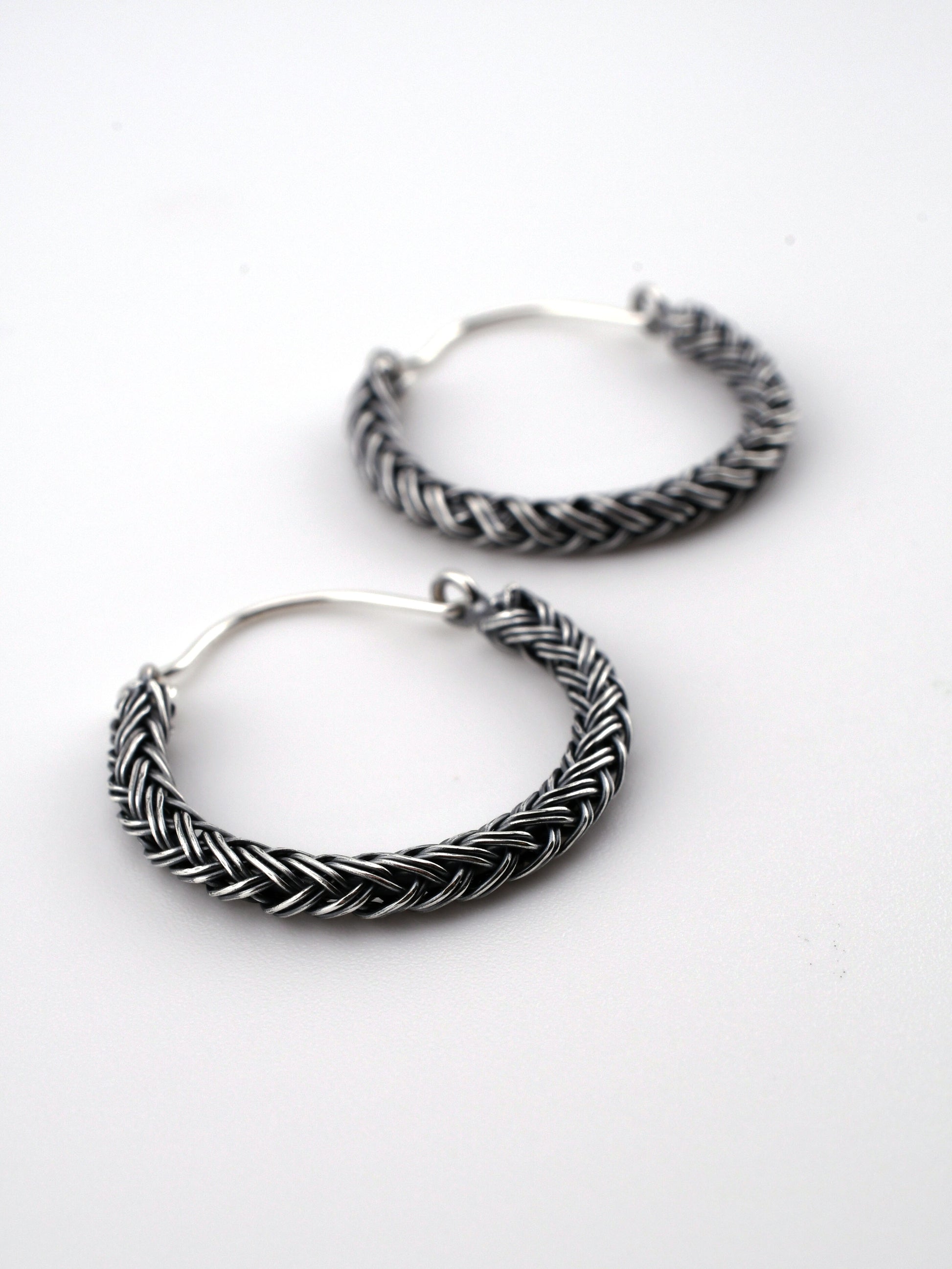 Pair of silver hoop earrings with braided design on a white background