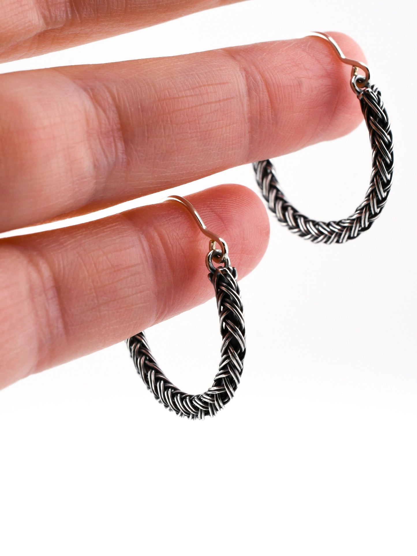 Silver braided hoop earrings held in a hand on a white background