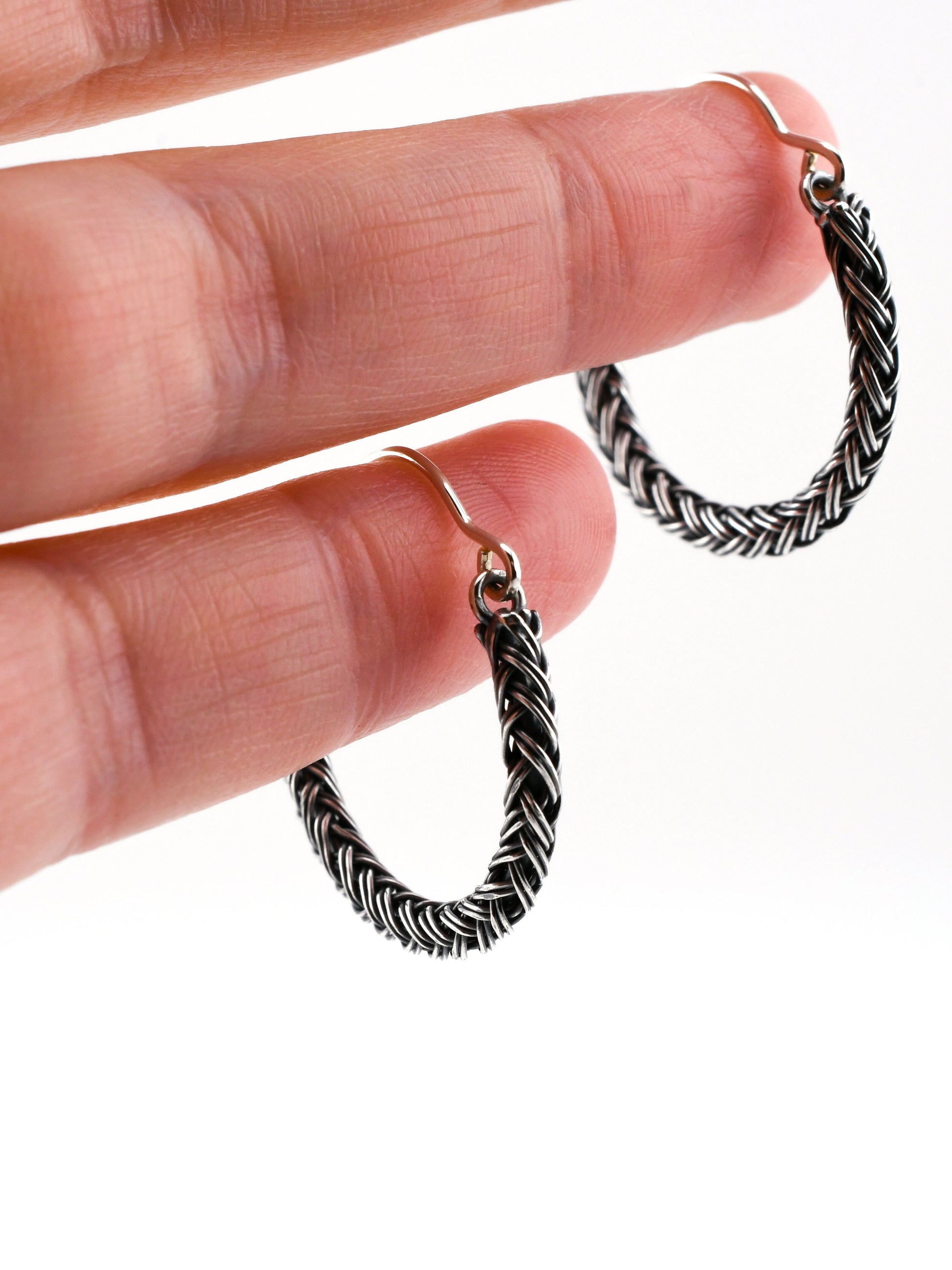 Silver braided hoop earrings held in a hand on a white background