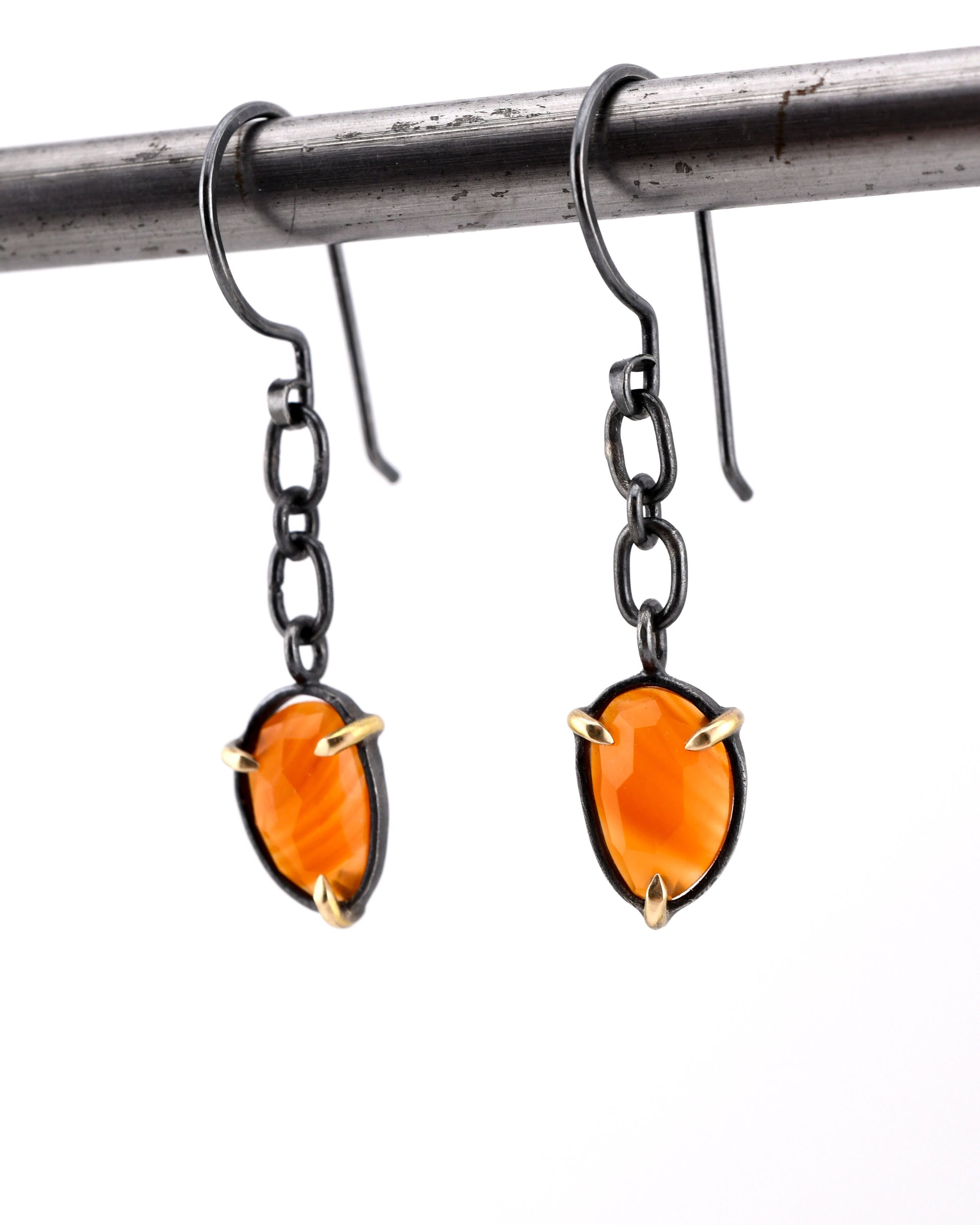 Pair of earrings with orange gemstones and black chains with 14k gold accents on a white background
