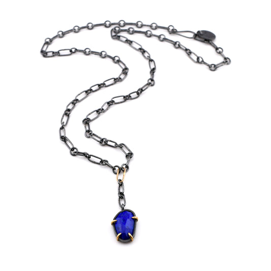Black silver chain necklace made from oval links with a blue lapis set in gold prongs displayed on a white background