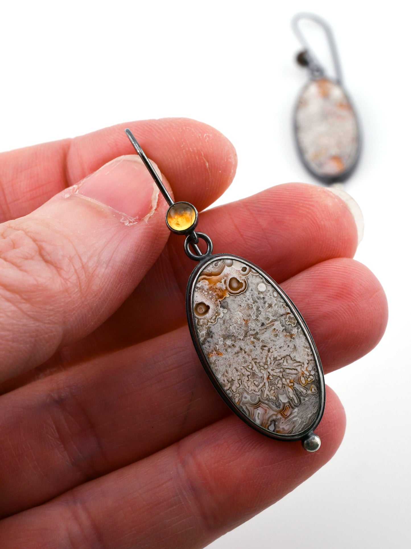 Close-up of a hand holding a unique earring with a natural stone design.