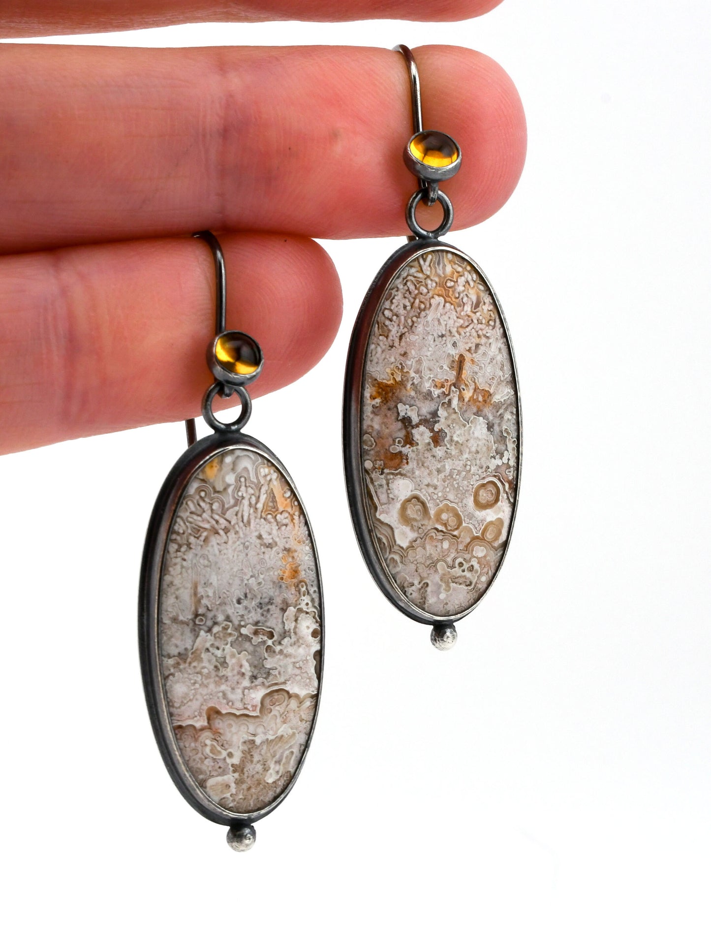 Oval-shaped earrings with a lacy design held between fingers against a white background