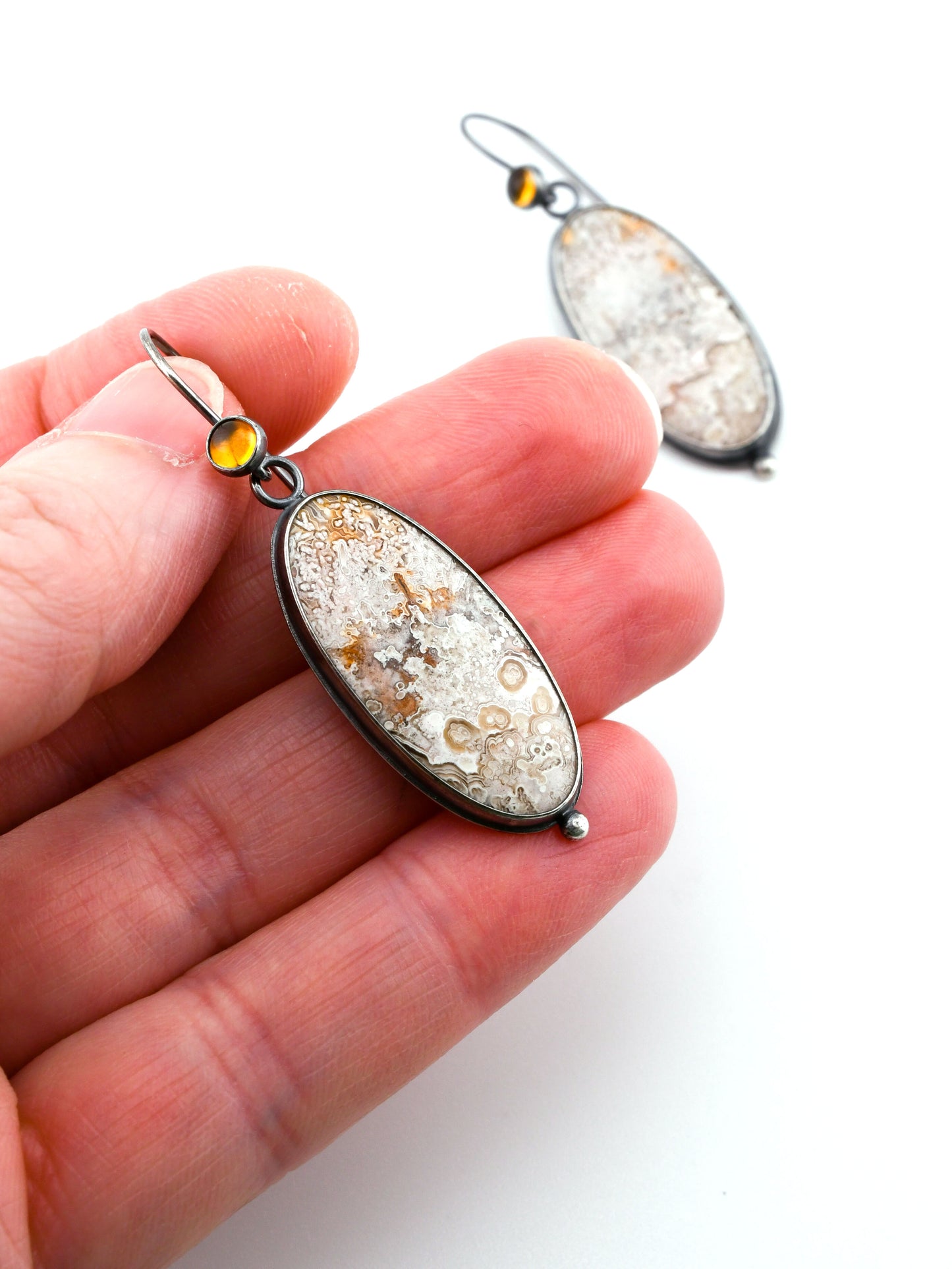 Close-up of a hand holding a decorative earring with a white background.