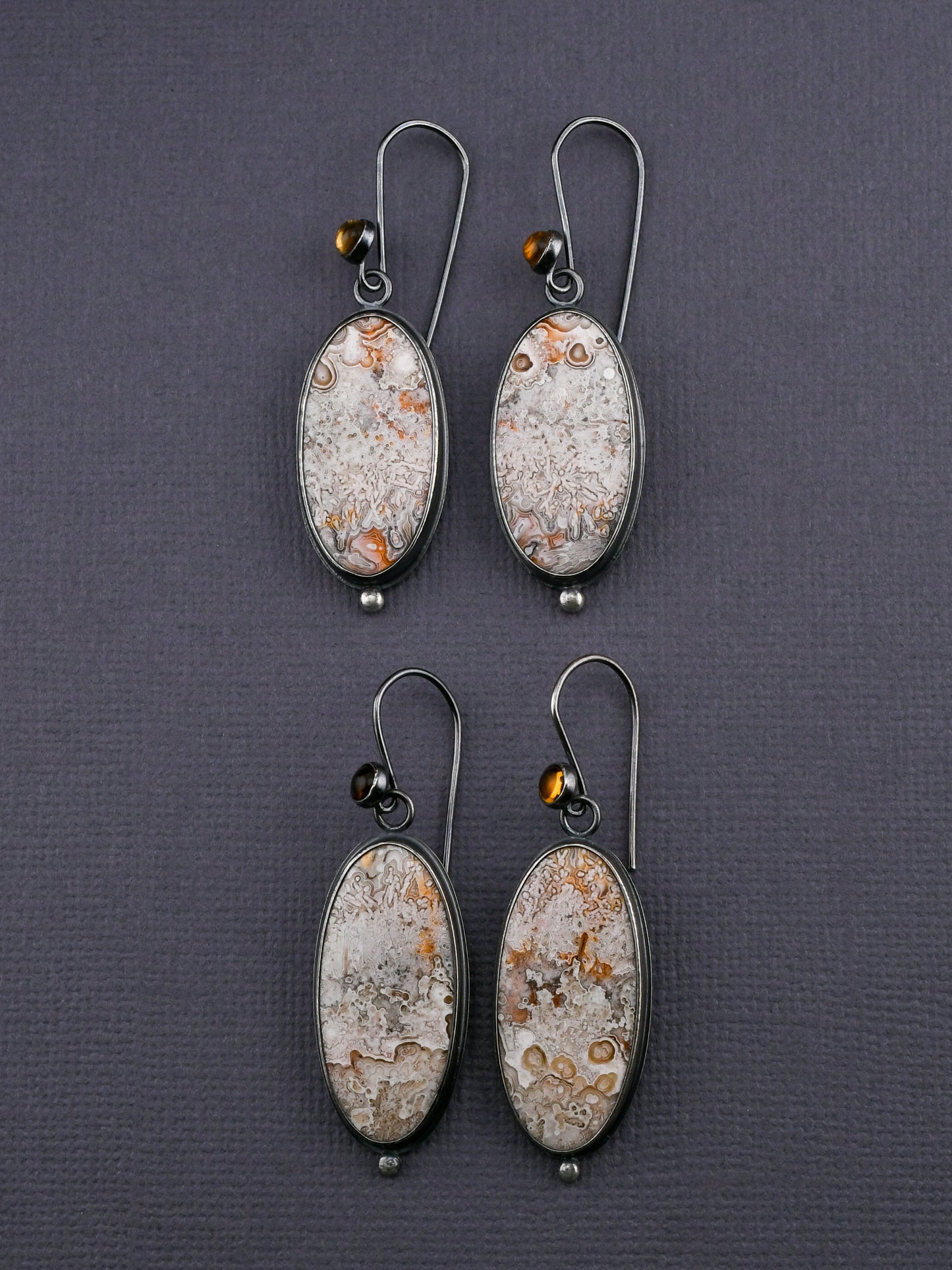 Two pairs of earrings with oval agates and citrines displayed on a dark gray background