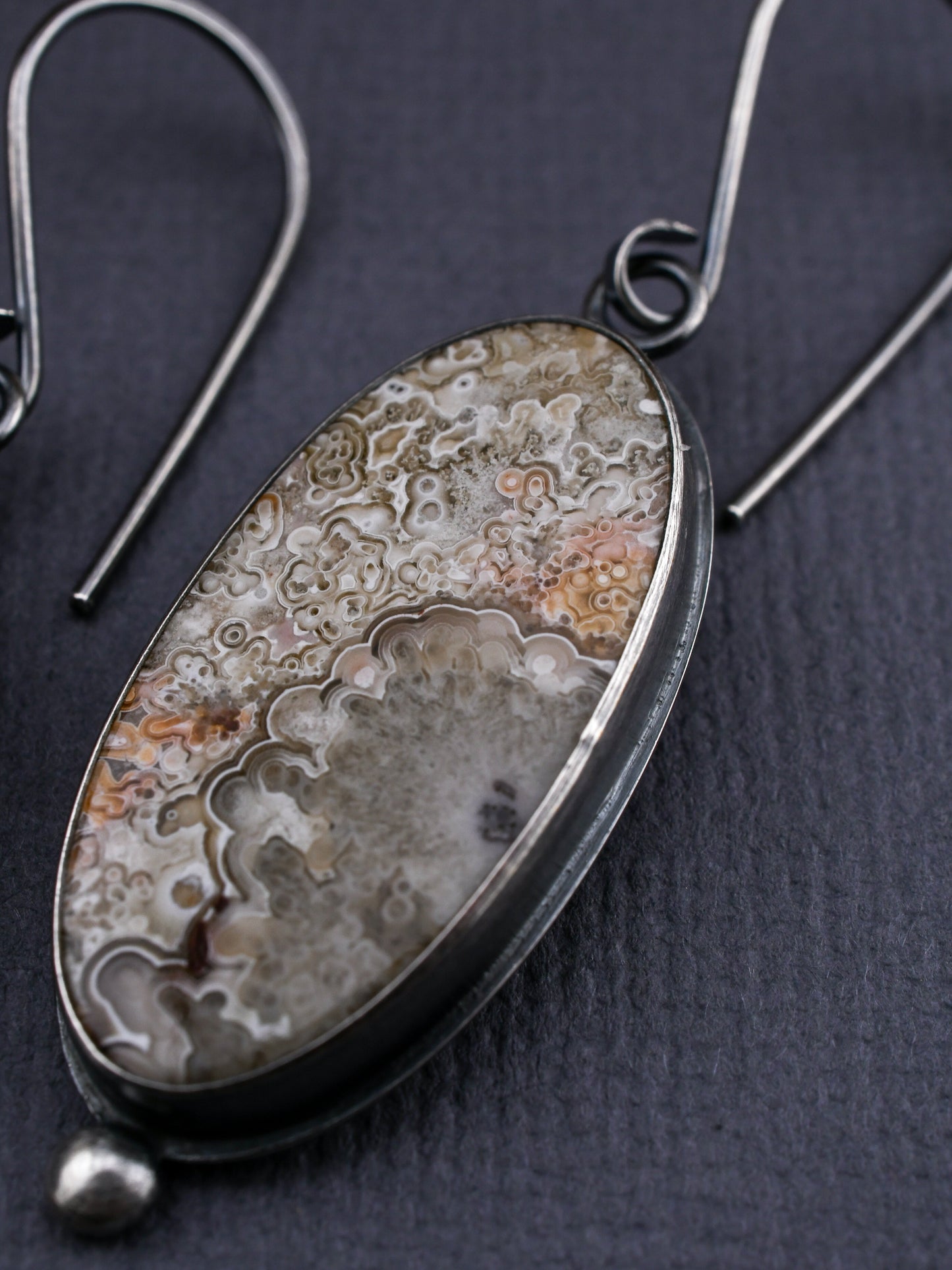 Oval-shaped earrings with silver and stone design on a dark background