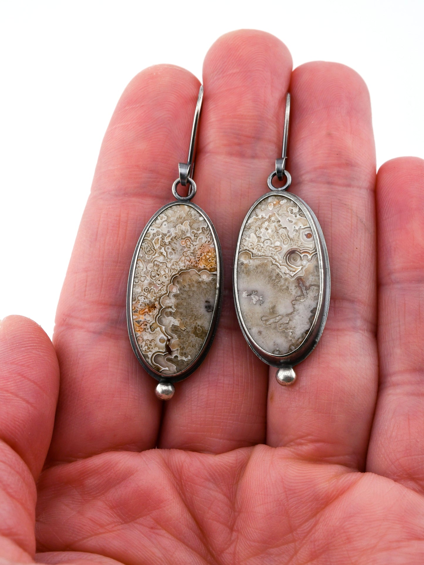 Pair of earrings with natural stone design held in hand against a white background