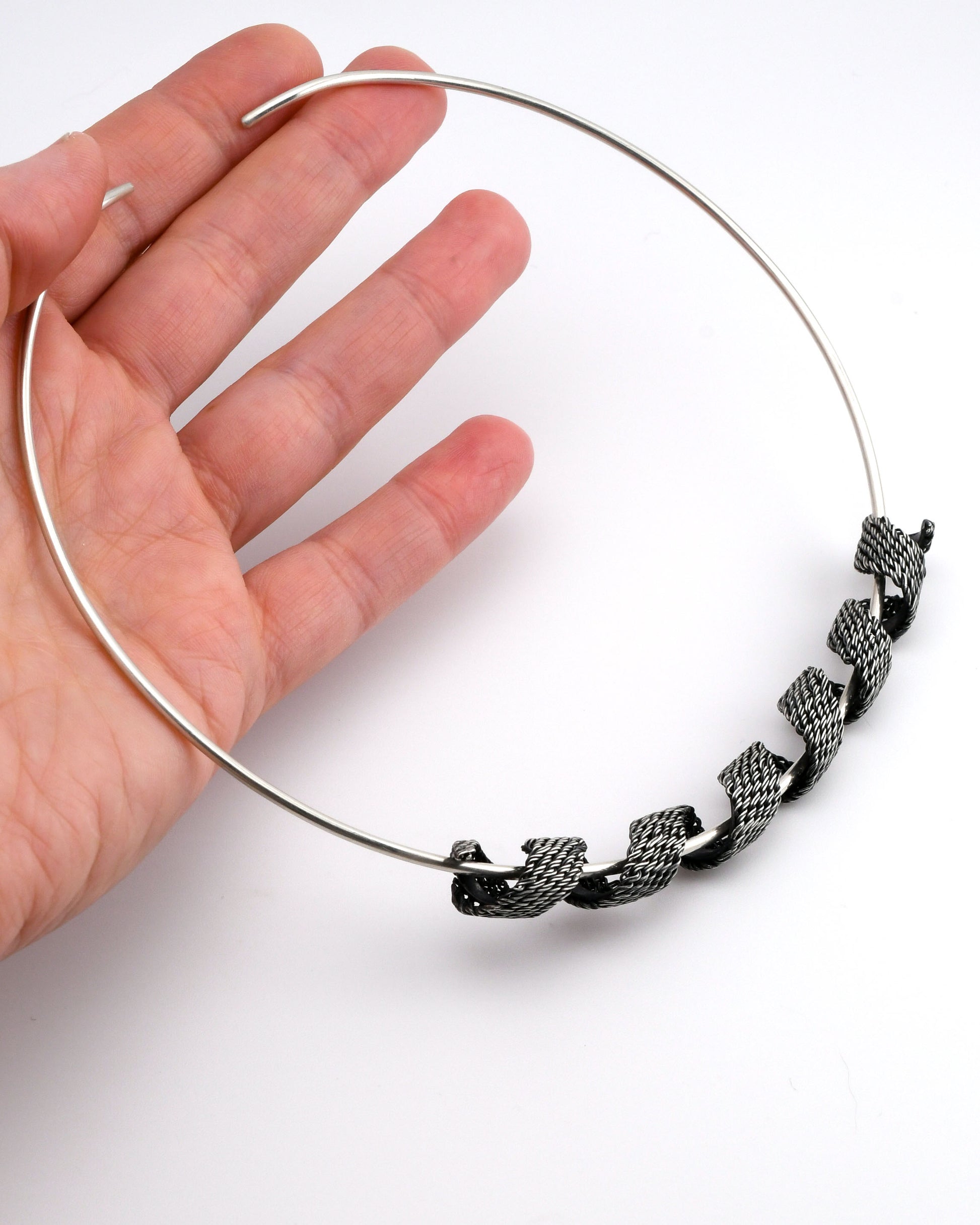 Silver torque necklace with woven silver coiled form held in a hand on a white background