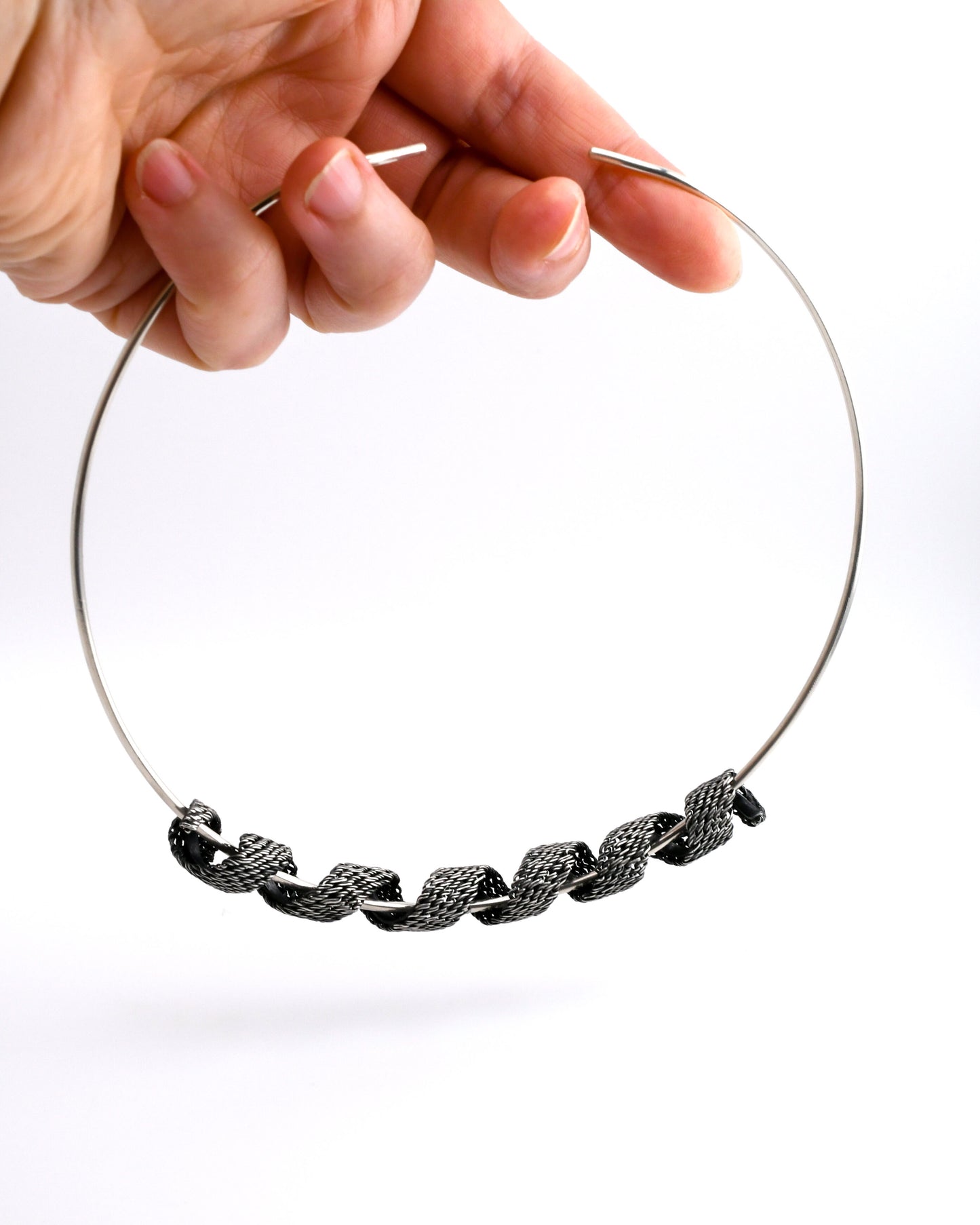 Silver torque necklace with woven silver coil suspended from a hand on a white background