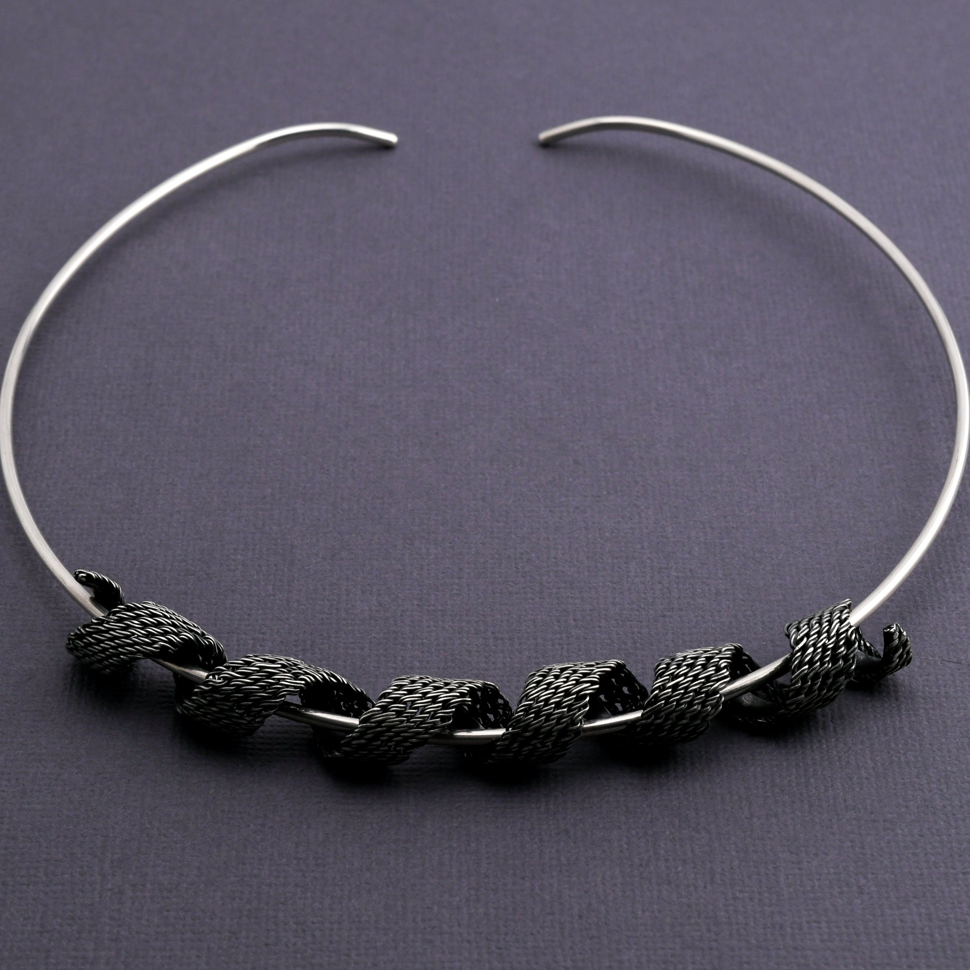 Silver torque necklace woven silver form coiled around the neckpiece on a dark gray background