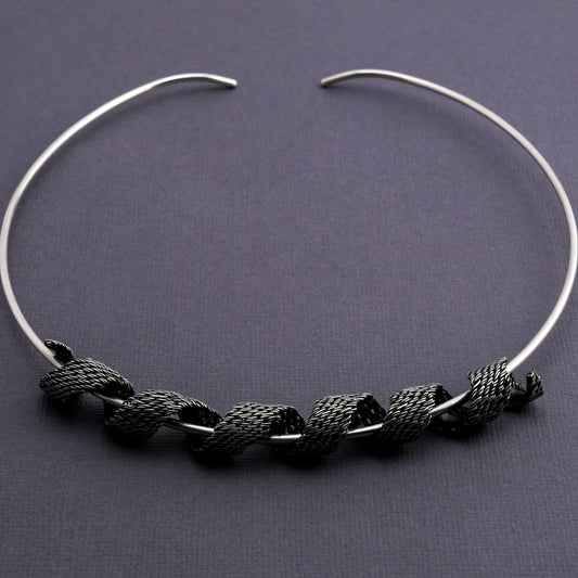 Silver torque necklace woven silver form coiled around the neckpiece on a dark gray background