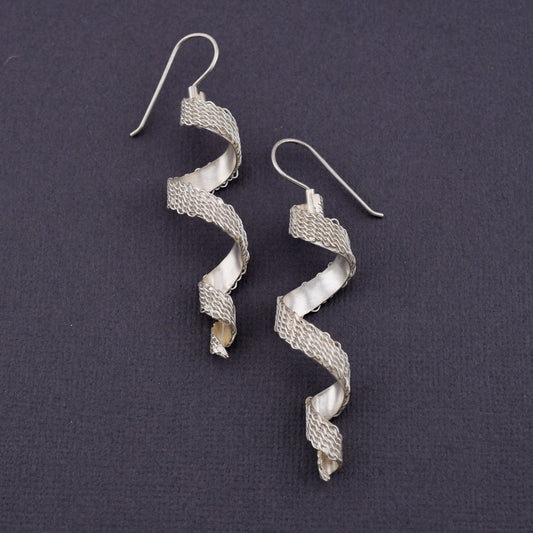 A pair of silver spiral drop earrings with a woven patterned spiral body and fishhook ear wires, displayed on a dark textured background.