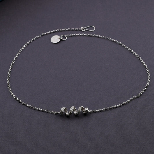 A woven silver coil necklace arranged on a dark gray textured background